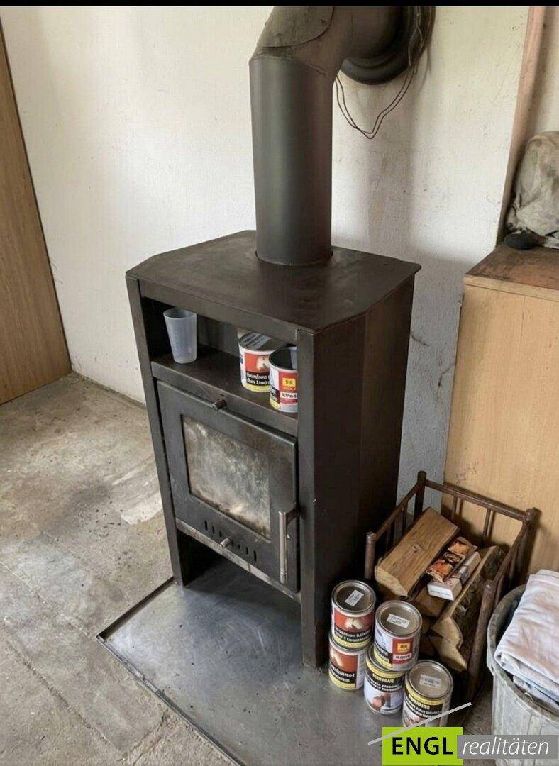 Detailaufnahme eines Holzofens mit Brennholz daneben, bereit zum Heizen.