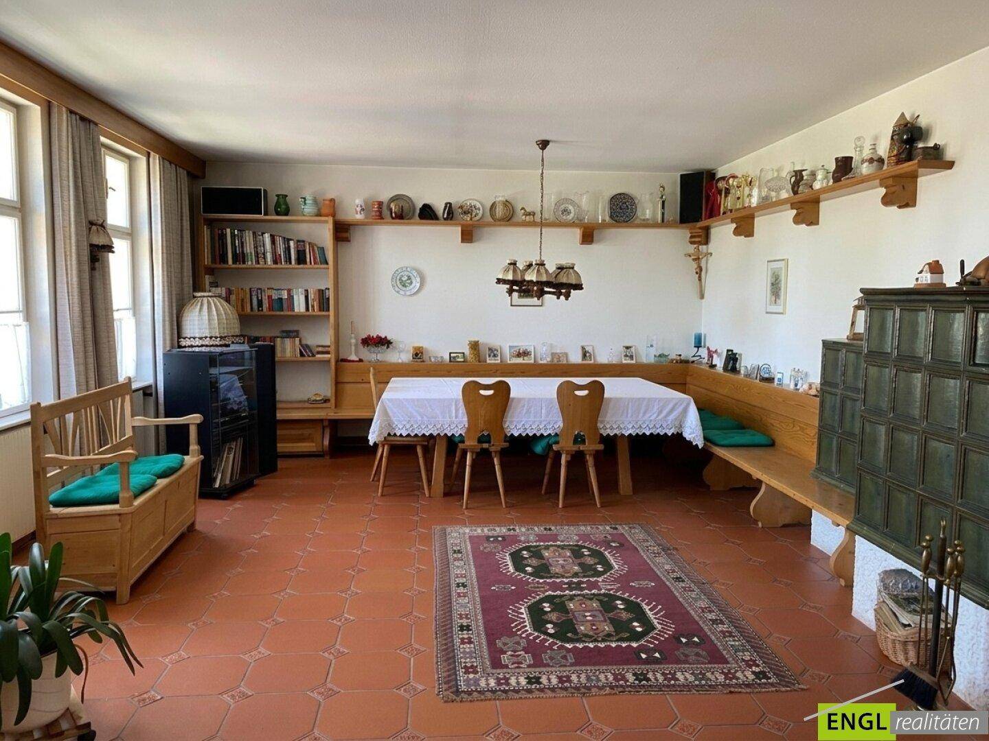 Traditioneller Essbereich mit Kachelofen, Holzbänken und Terrakotta-Boden, gemütlich eingerichtet.