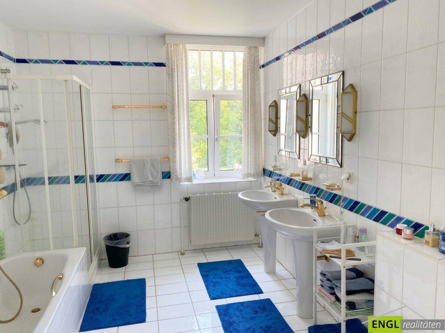 Helles Badezimmer mit weißen Fliesen, blauen Akzenten, Doppelwaschbecken und Badewanne.