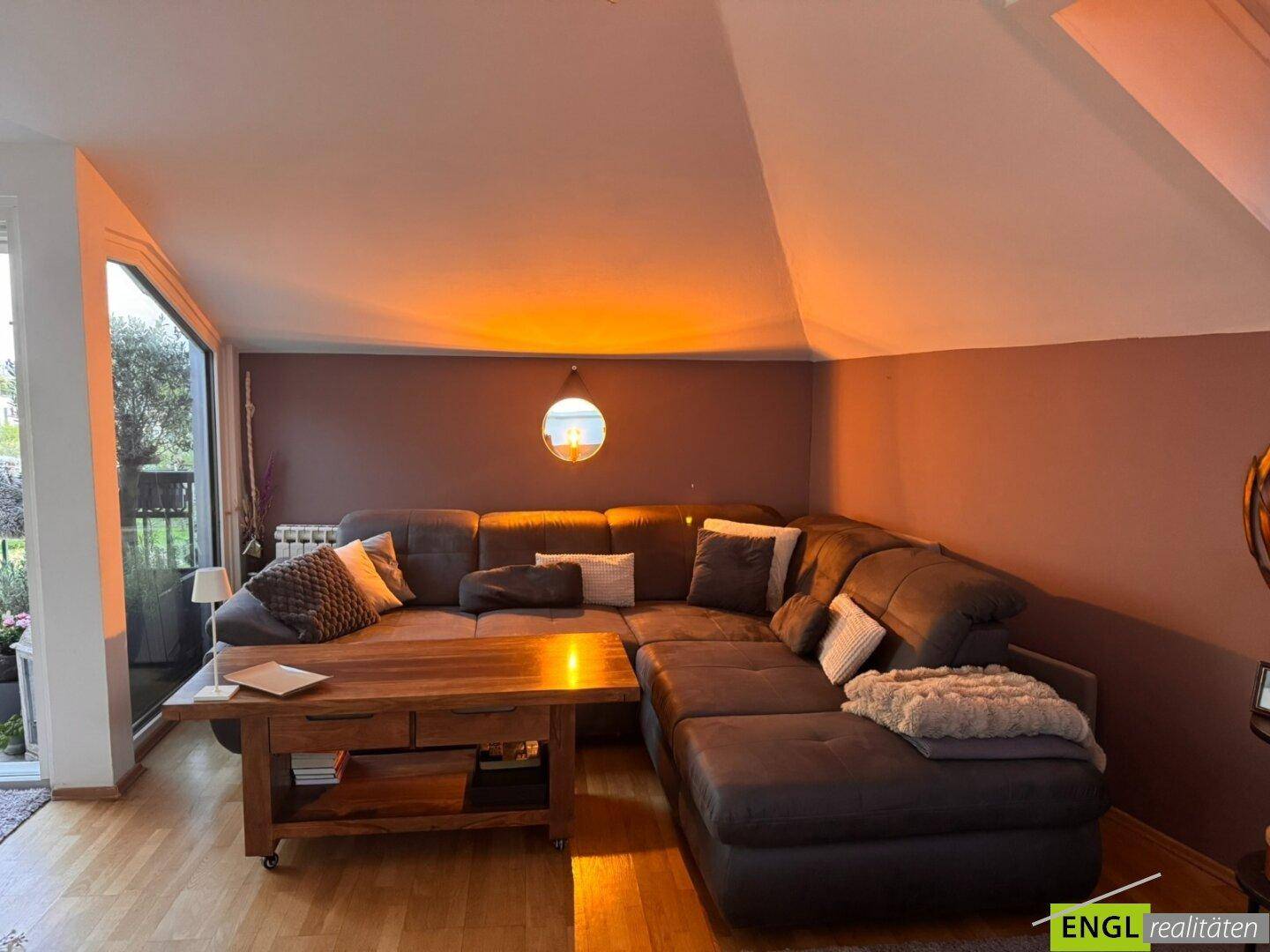 Gemütliches Wohnzimmer mit großem Ecksofa, Holztisch und Zugang zum Balkon.