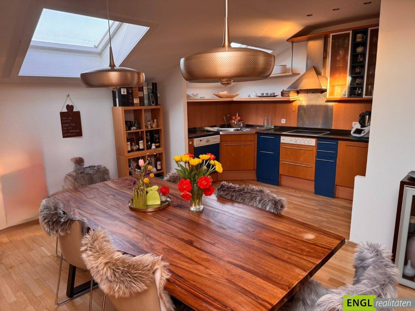 Offener Wohn- und Essbereich mit großem Holztisch und integrierter Küche im Hintergrund.