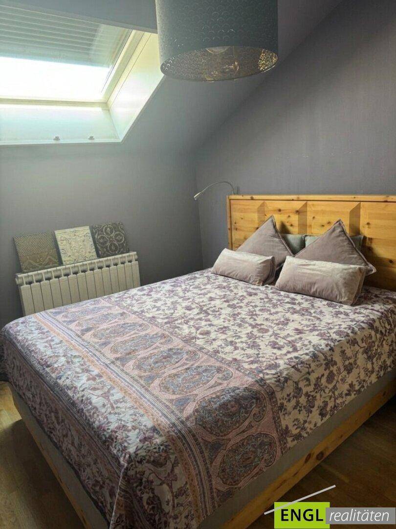 Gemütliches Schlafzimmer mit Holzbett, gemusterter Bettwäsche und einem Dachfenster.