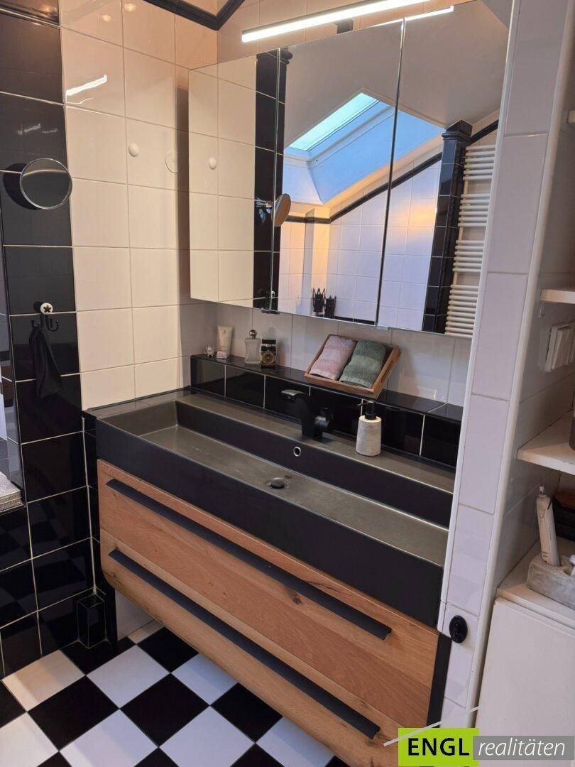 Modernes Badezimmer mit schwarz-weißen Fliesen, Doppelwaschbecken und Dachfenster.