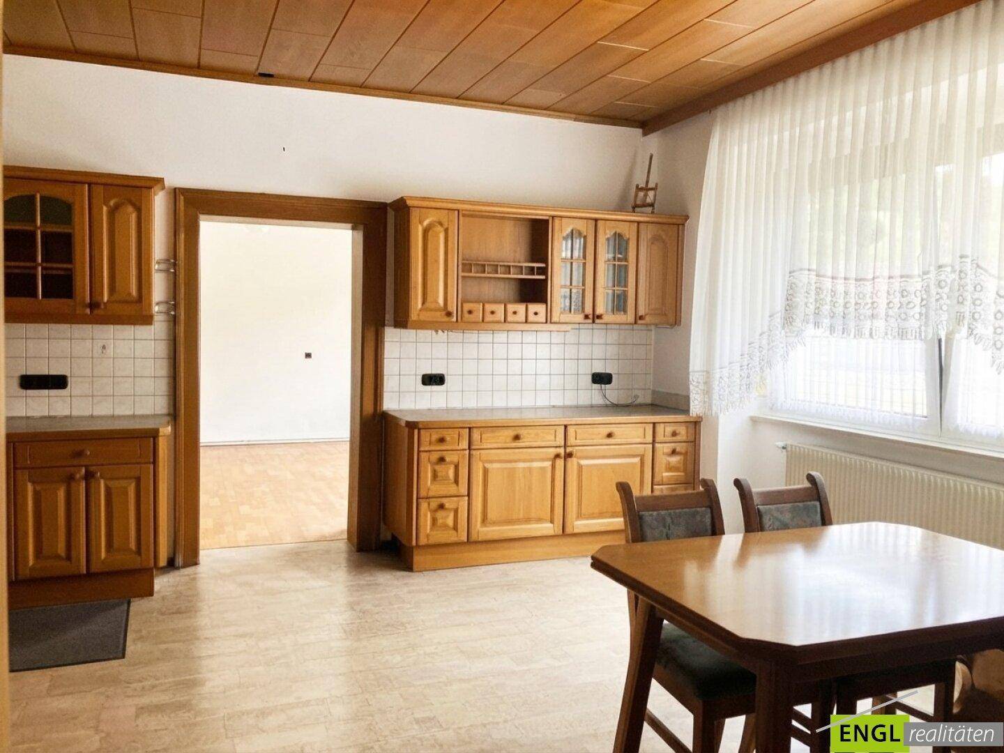 Gemütliche Wohnküche mit Holzeinrichtung, Esstisch und einem Fenster, das Tageslicht hereinlässt.