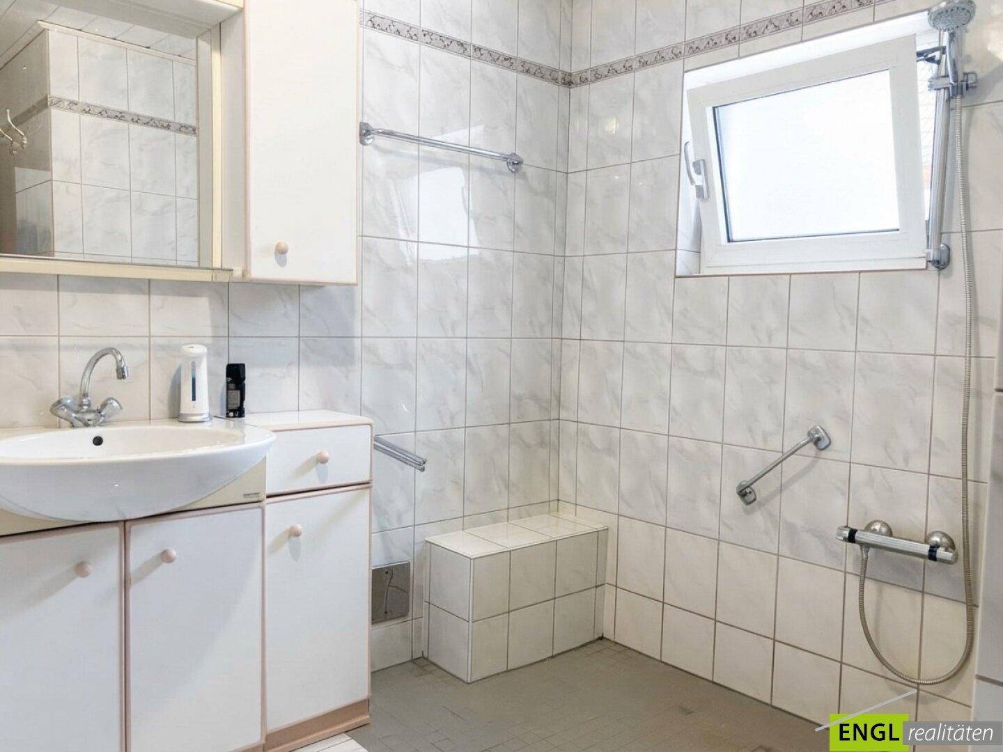 Gefliestes Badezimmer mit Waschbecken, Duschbereich und Haltegriffen für zusätzliche Sicherheit.