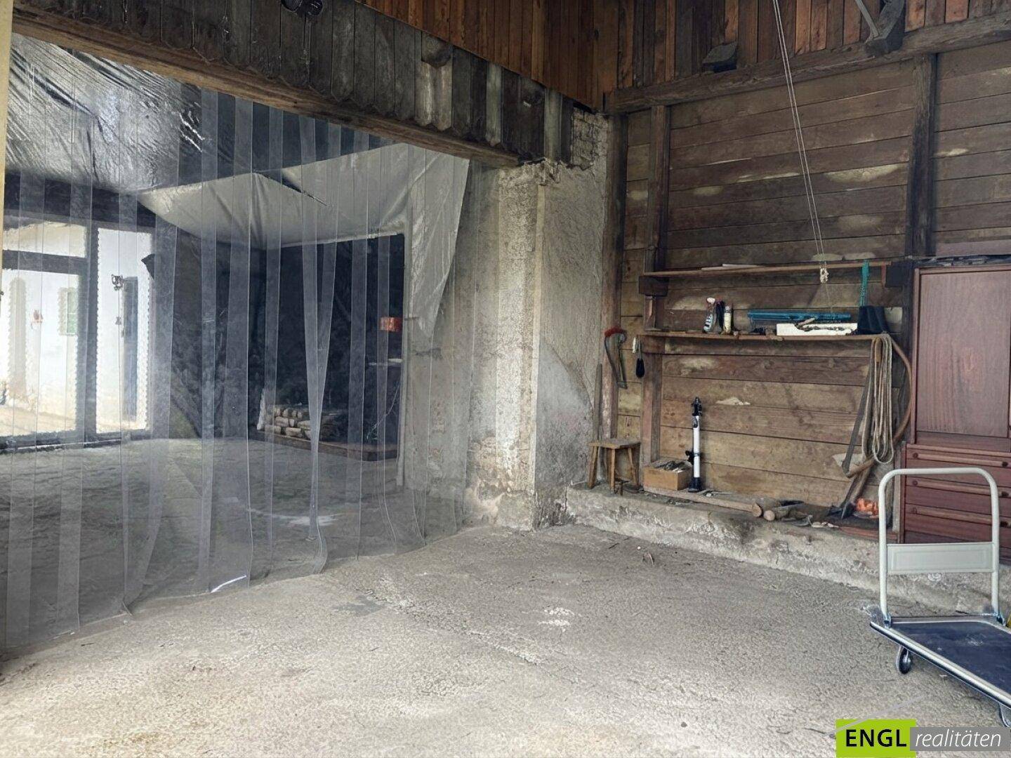 Rustikaler Innenraum, möglicherweise eine Werkstatt oder Scheune, mit Holzwänden und Betonboden.
