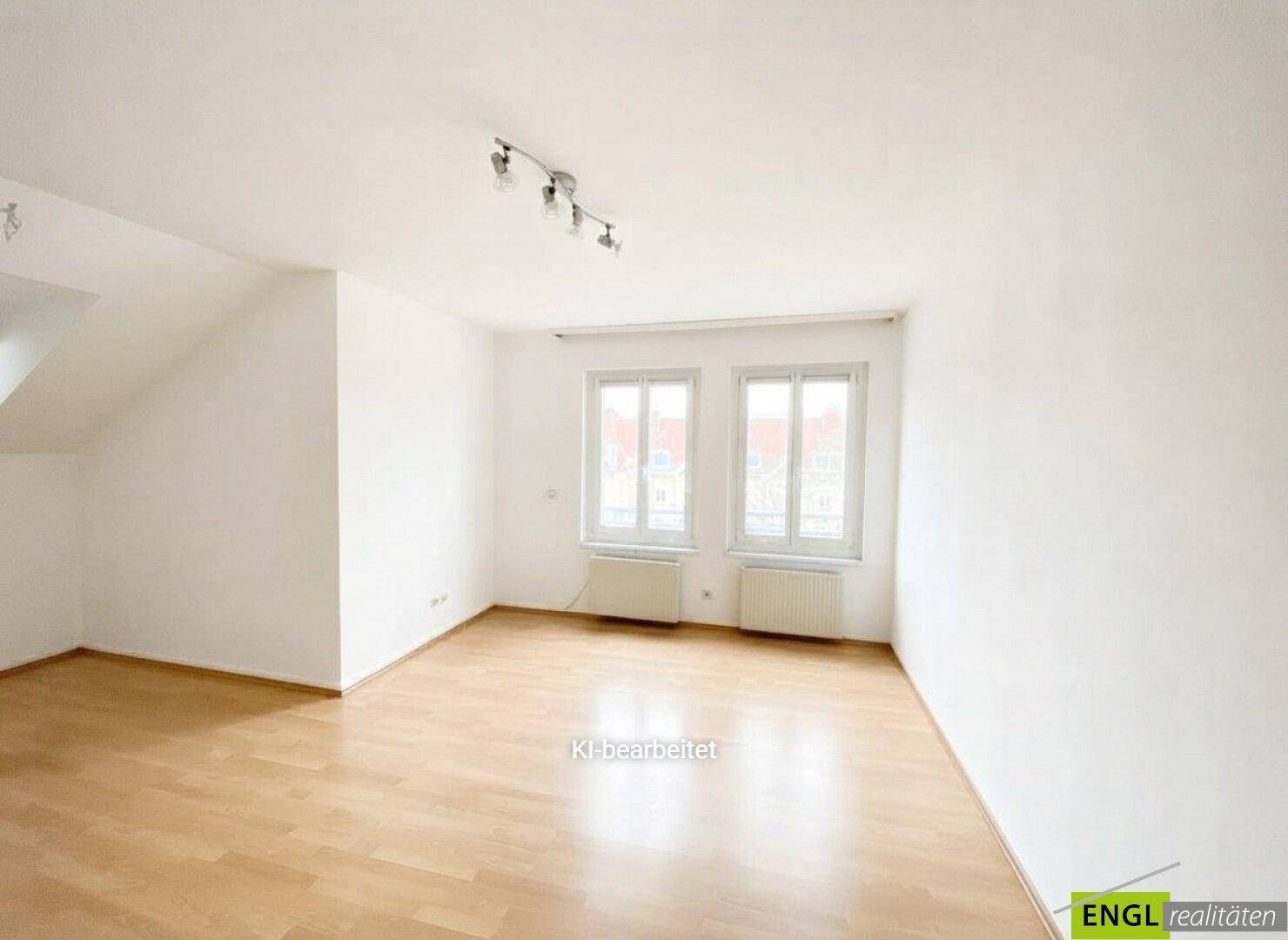 Leeres, helles Zimmer mit Holzboden, großen Fenstern und Dachschräge.