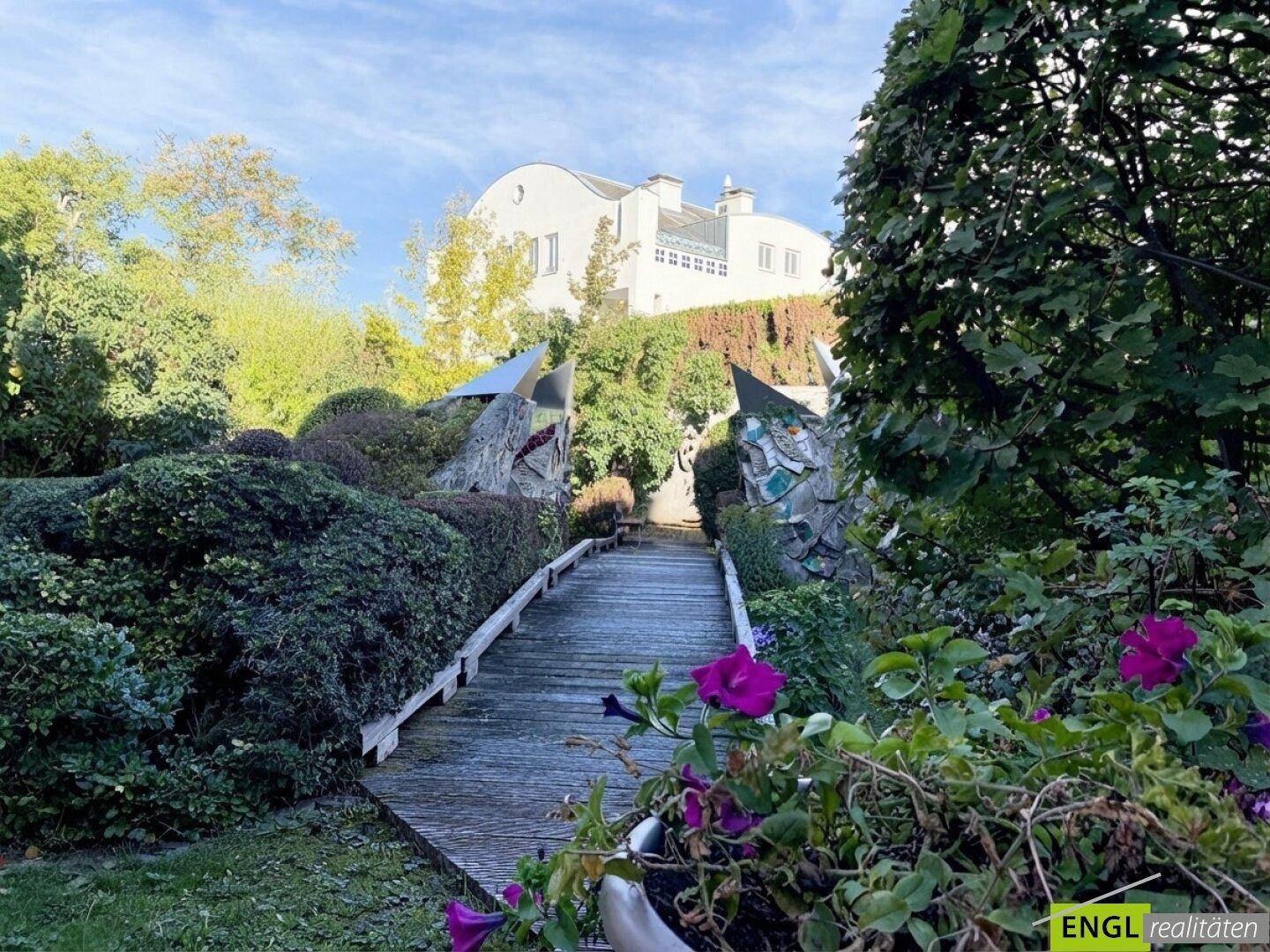 Malerischer Gartenweg führt zu einem einzigartigen Gebäude mit weißer Fassade im Hintergrund.