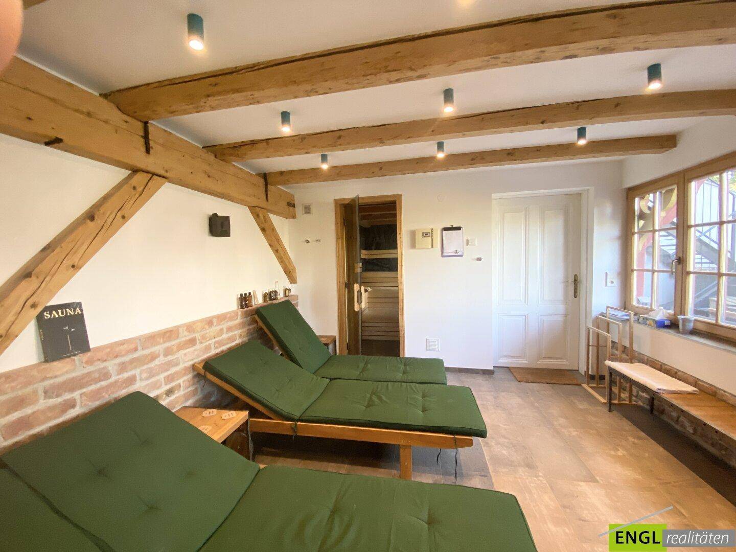 Entspannungsbereich mit sichtbaren Holzbalken, Liegestühlen und einer angrenzenden Sauna.