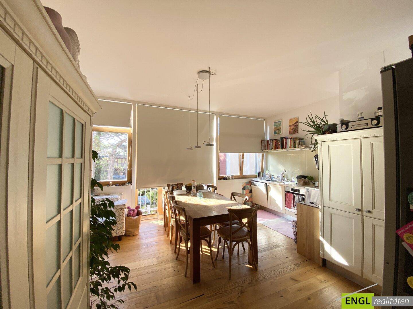 Geräumige Wohnküche mit Essbereich, Holzboden und viel Tageslicht durch die Fenster.
