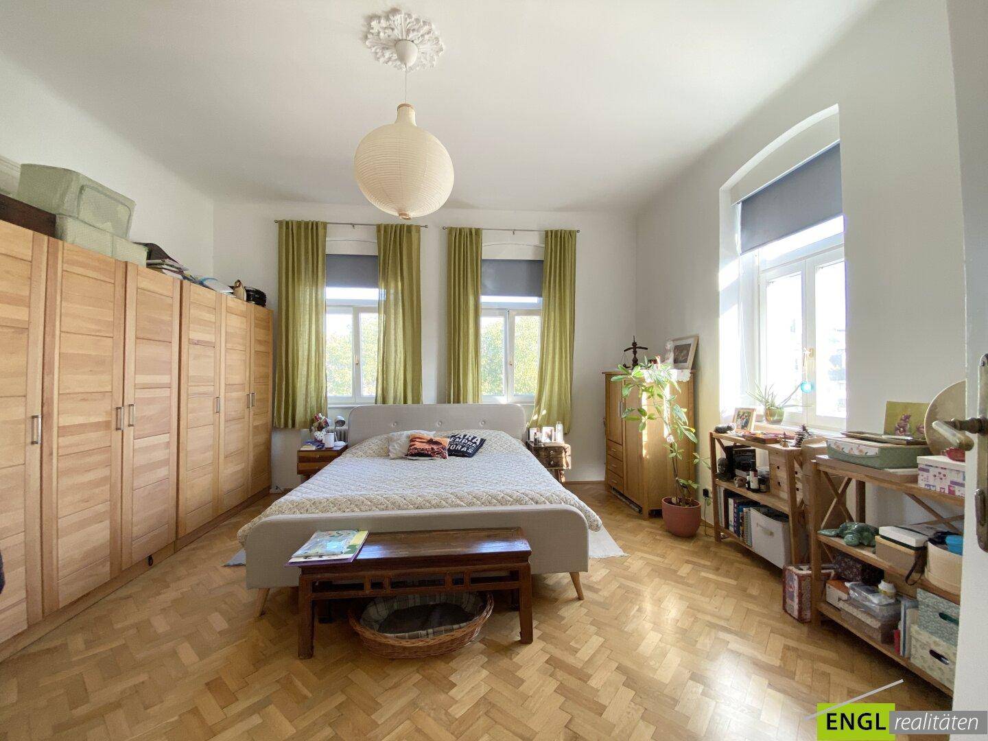 Helles Schlafzimmer mit Fischgrätparkett, großen Holzschränken und zwei Fenstern.