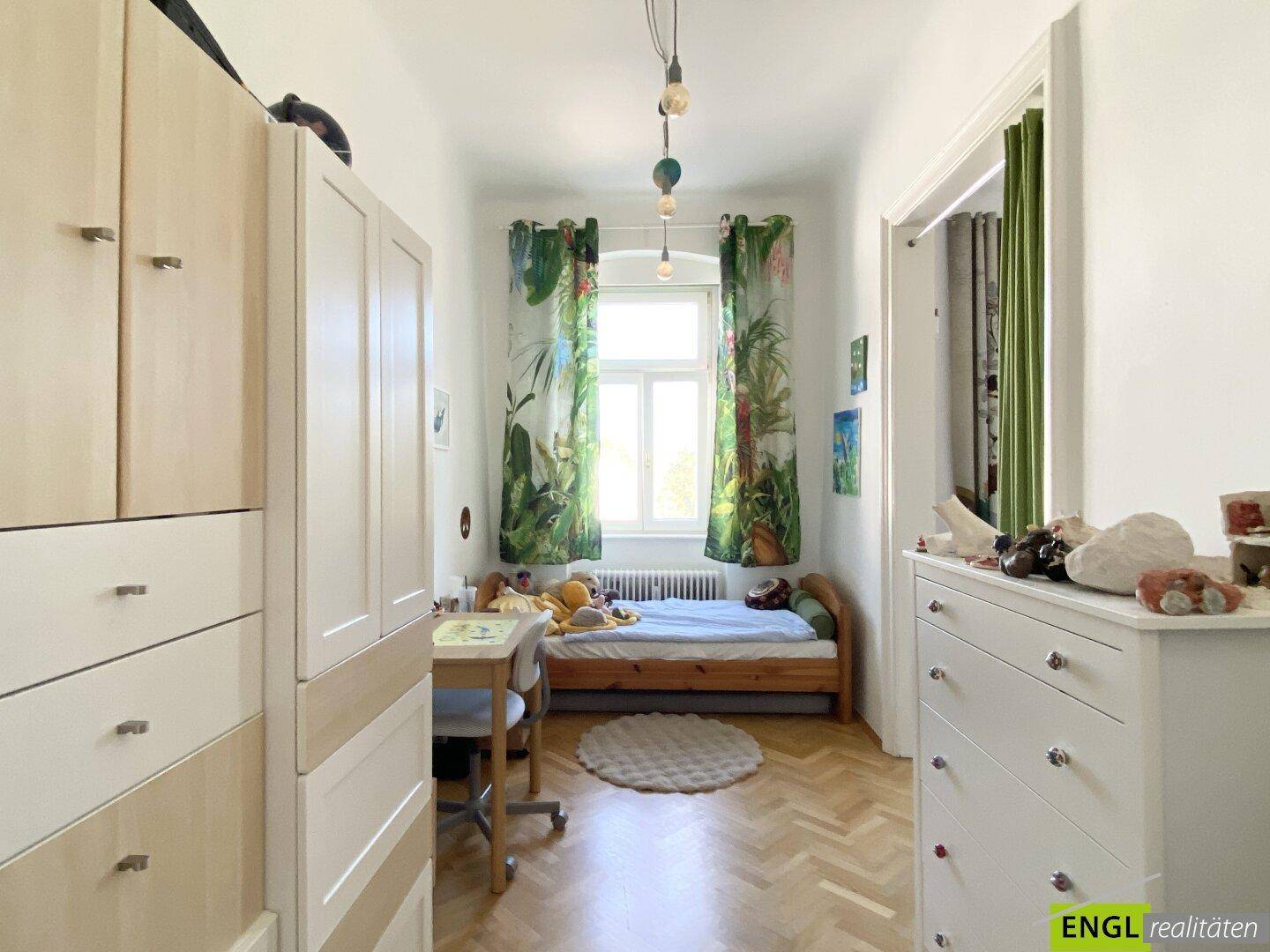 Gemütliches Kinderzimmer mit Holzboden, Einzelbett und farbenfrohen Vorhängen am Fenster.