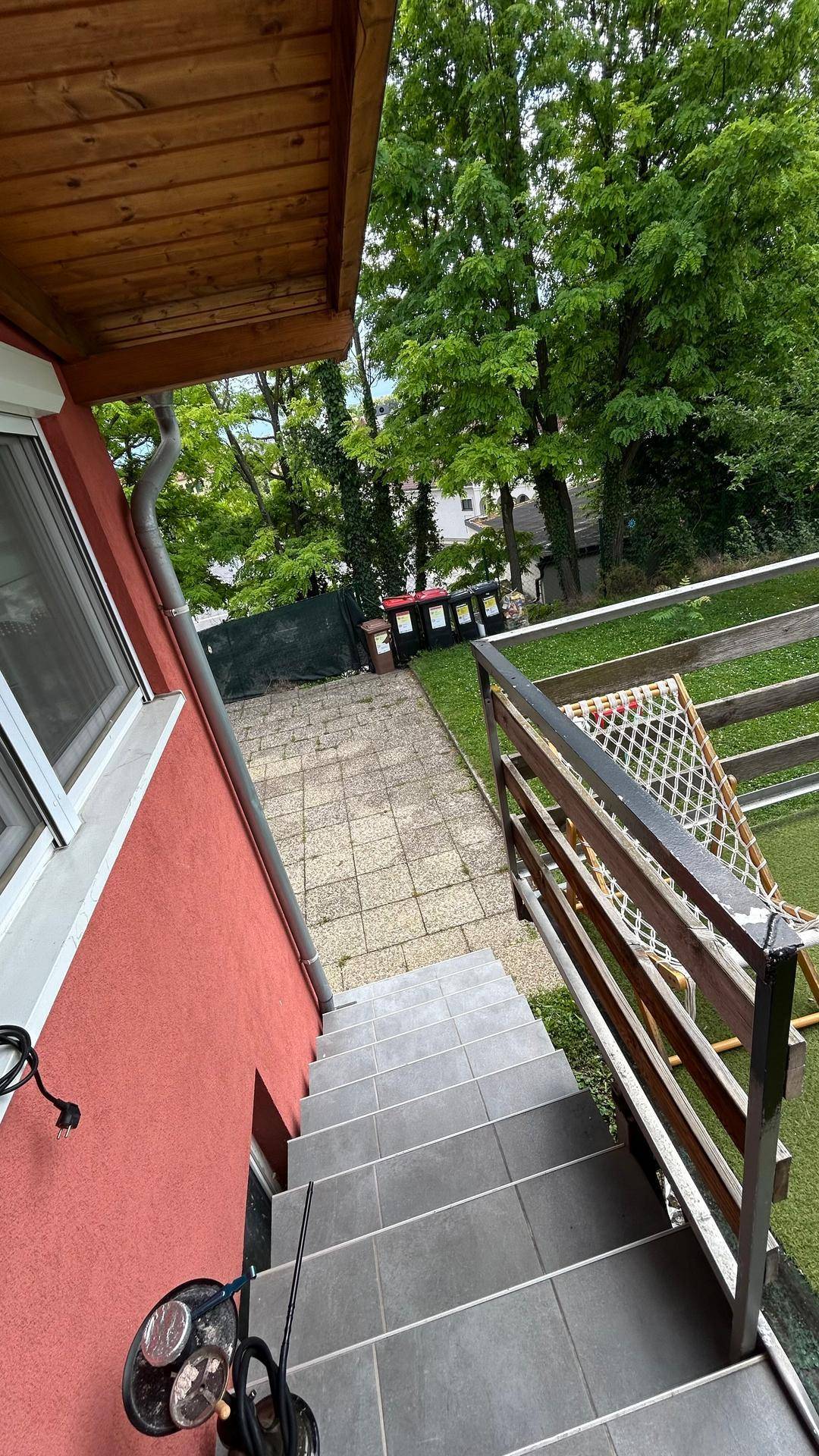 Außenansicht des Gebäudes mit Treppe, die zu einem gepflasterten Bereich und Garten führt.