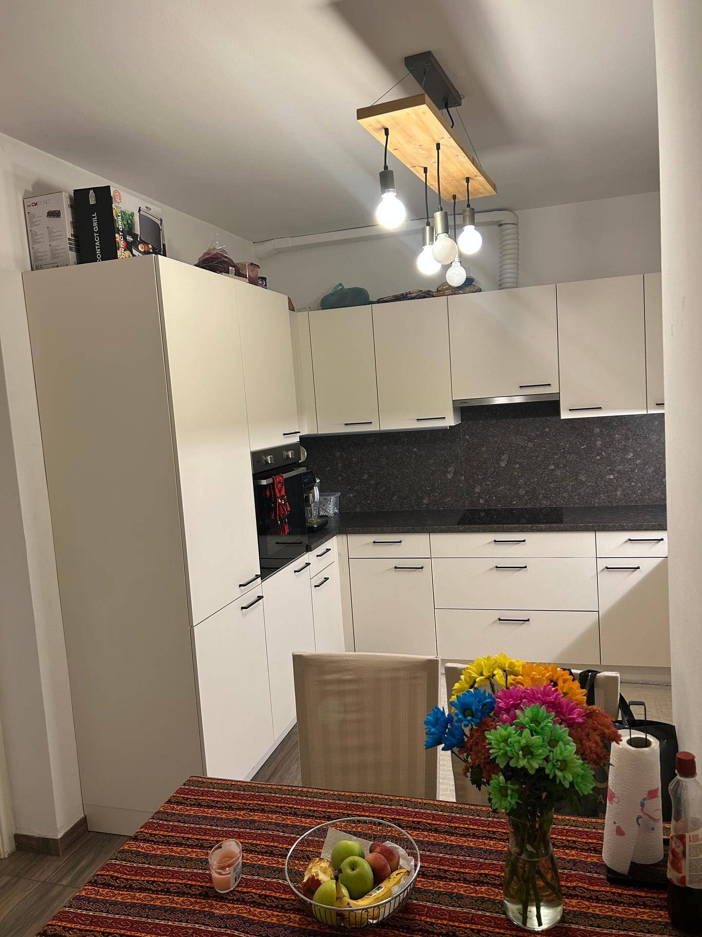 Moderne Küche mit weißen Schränken und dunkler Arbeitsplatte, Essbereich im Vordergrund.