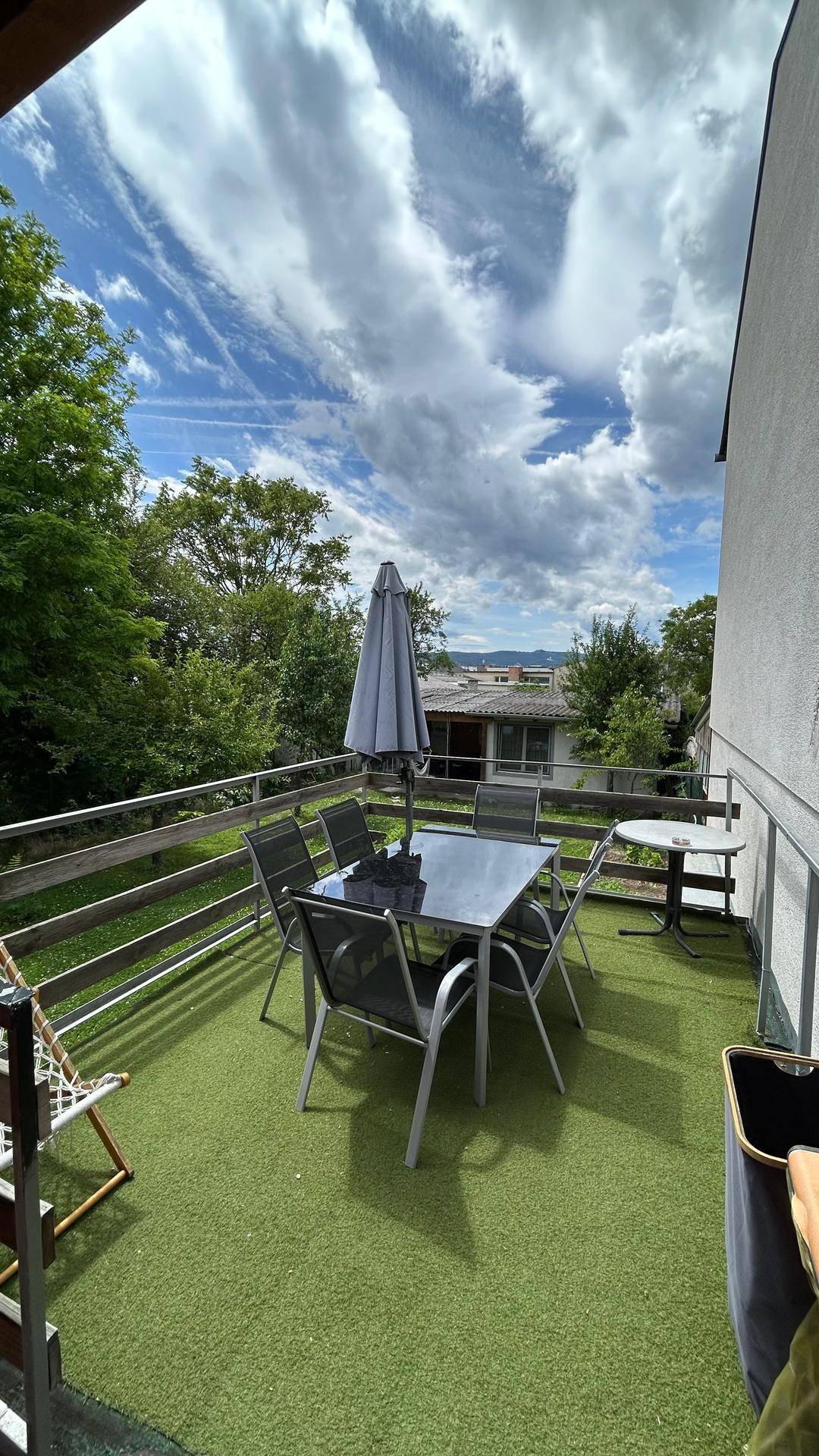 Große Terrasse mit Kunstrasen und Essbereich, umgeben von Bäumen und Häusern.
