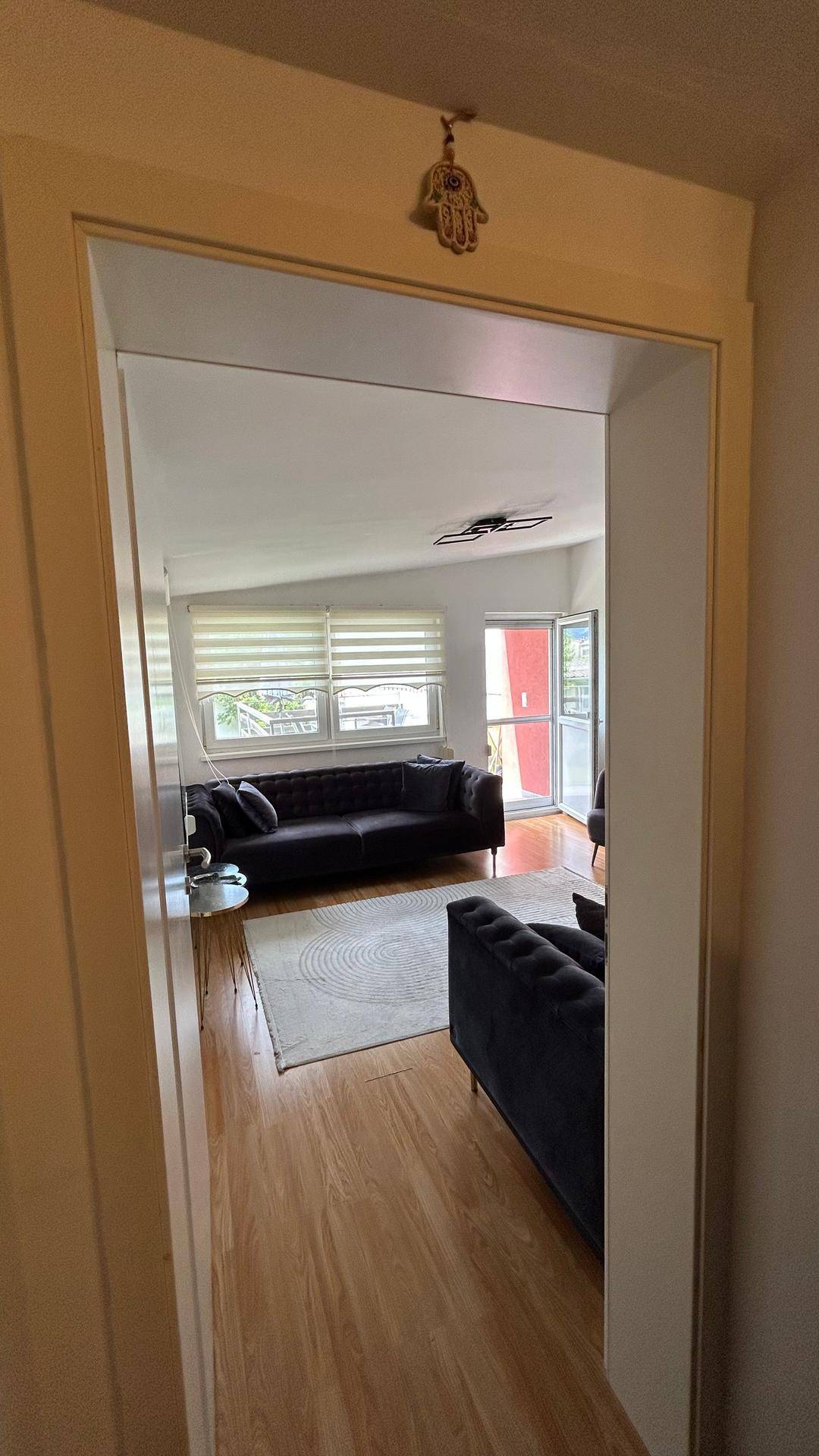 Blick vom Flur in das helle Wohnzimmer mit dunklen Sofas und Holzboden.