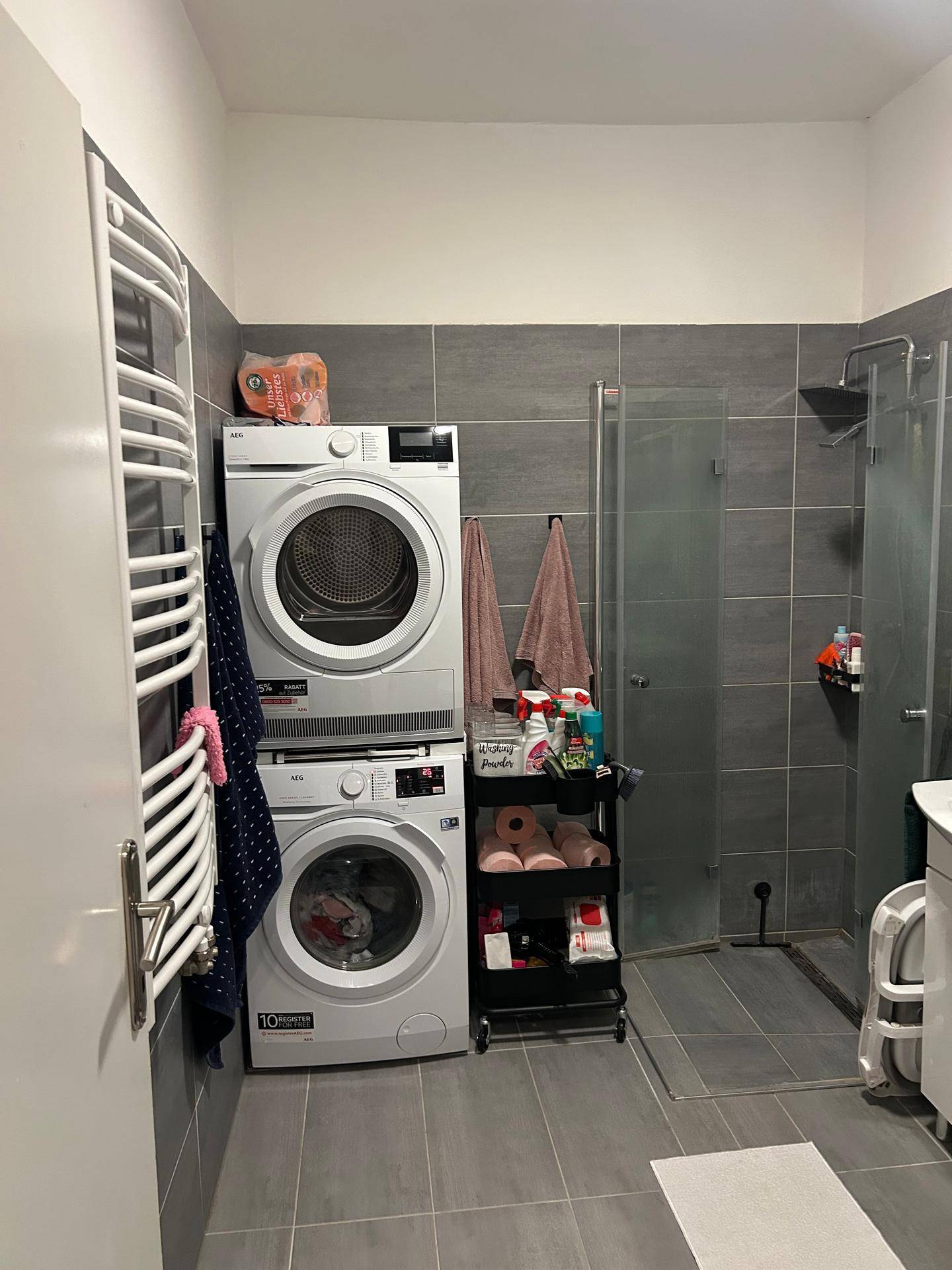 Badezimmer mit Dusche, Waschmaschine, Trockner und einem praktischen Handtuchheizkörper.