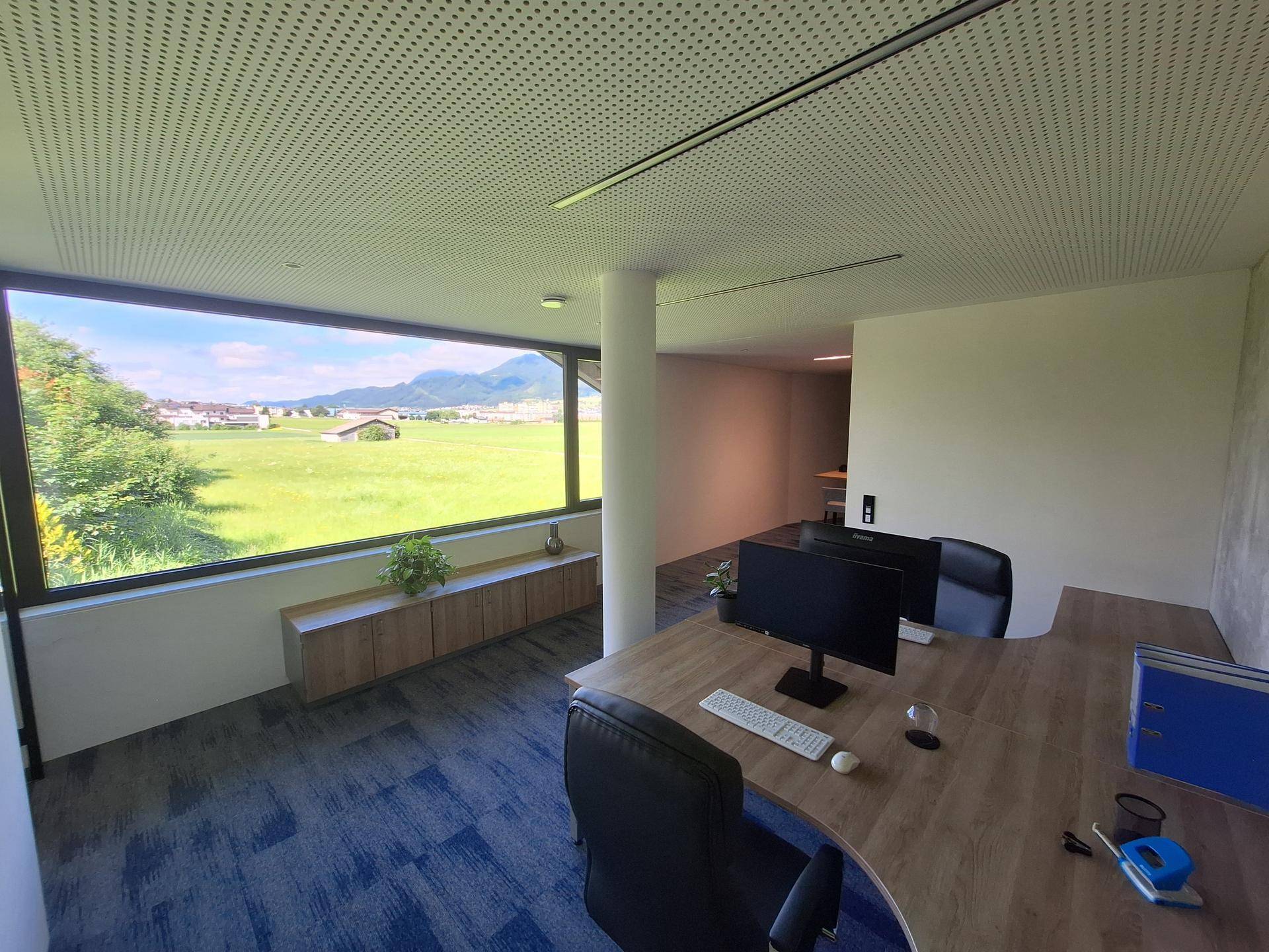 Großzügiges Büro mit mehreren Arbeitsplätzen, weitem Ausblick auf die Landschaft und moderne Deckenbeleuchtung.