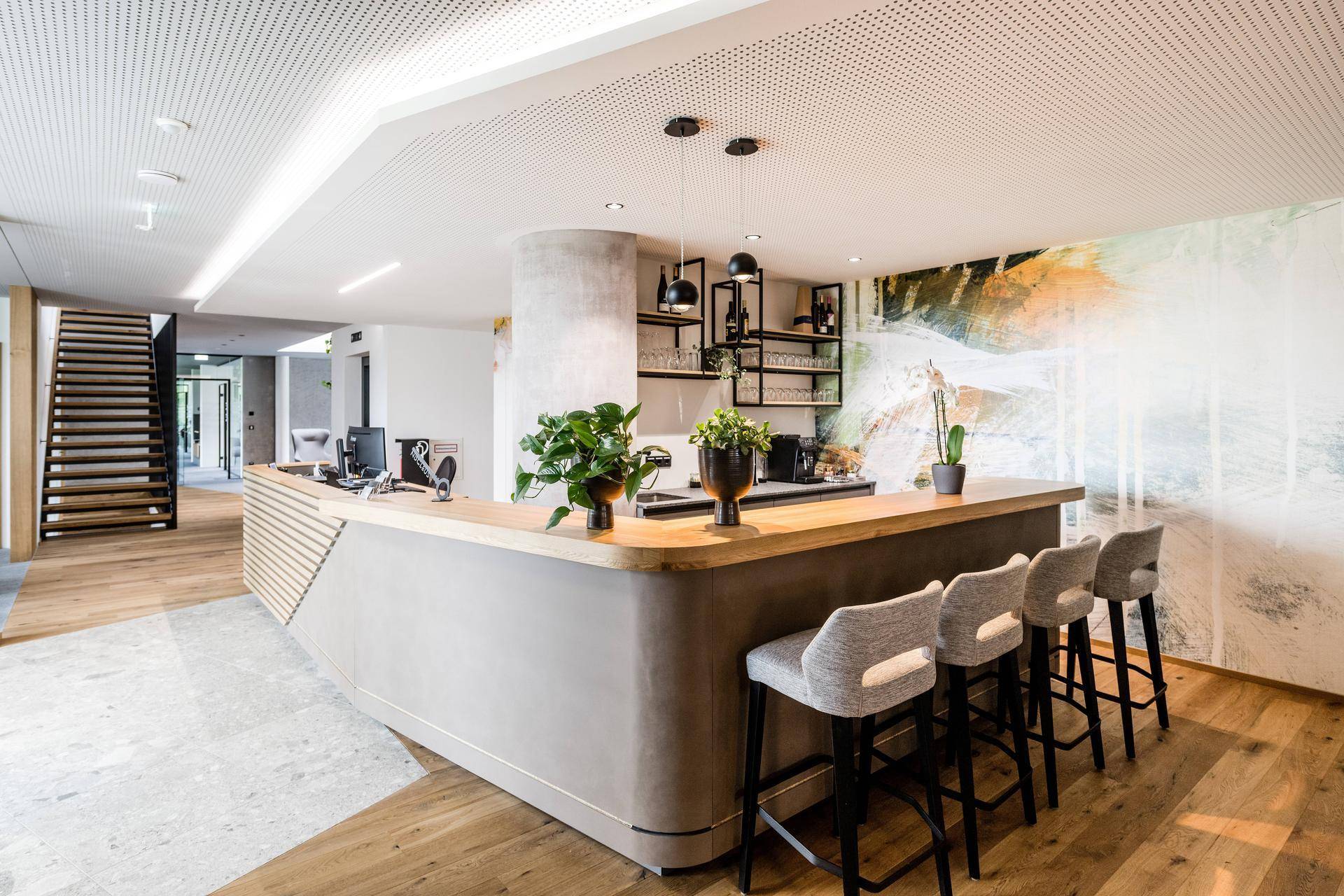 Moderne Lounge-Bar mit geschwungener Theke, Barhockern und einer stilvollen Treppe im Hintergrund.