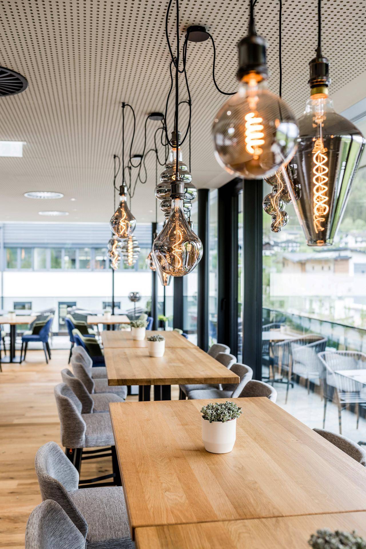 Stilvoller Restaurantbereich mit Holztischen, bequemen Stühlen und dekorativen Edison-Glühbirnen.