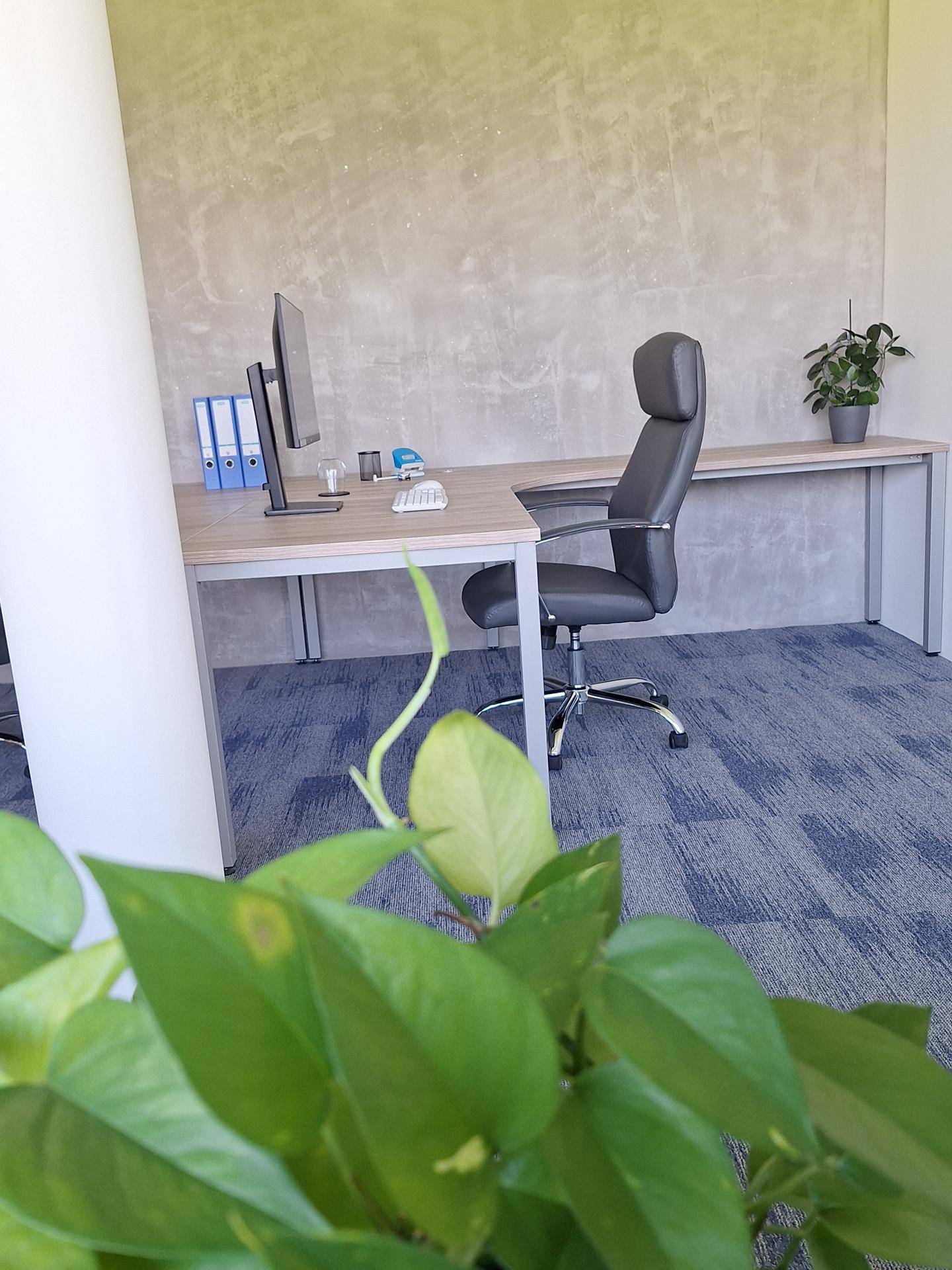 Geräumiges Büro mit L-förmigem Schreibtisch, ergonomischem Stuhl und modernem Teppichboden.