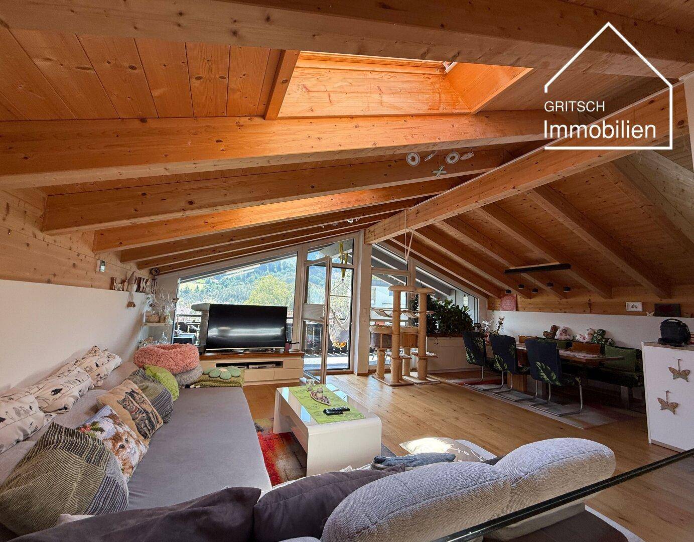 Gemütlicher Wohn-Essbereich im Dachgeschoss mit Holzbalken, Dachfenstern und Zugang zu einem Balkon.