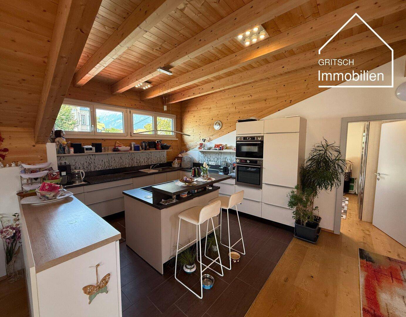 Moderne Einbauküche mit Kochinsel, hochwertigen Geräten und Holzbalkendecke im Dachgeschoss.
