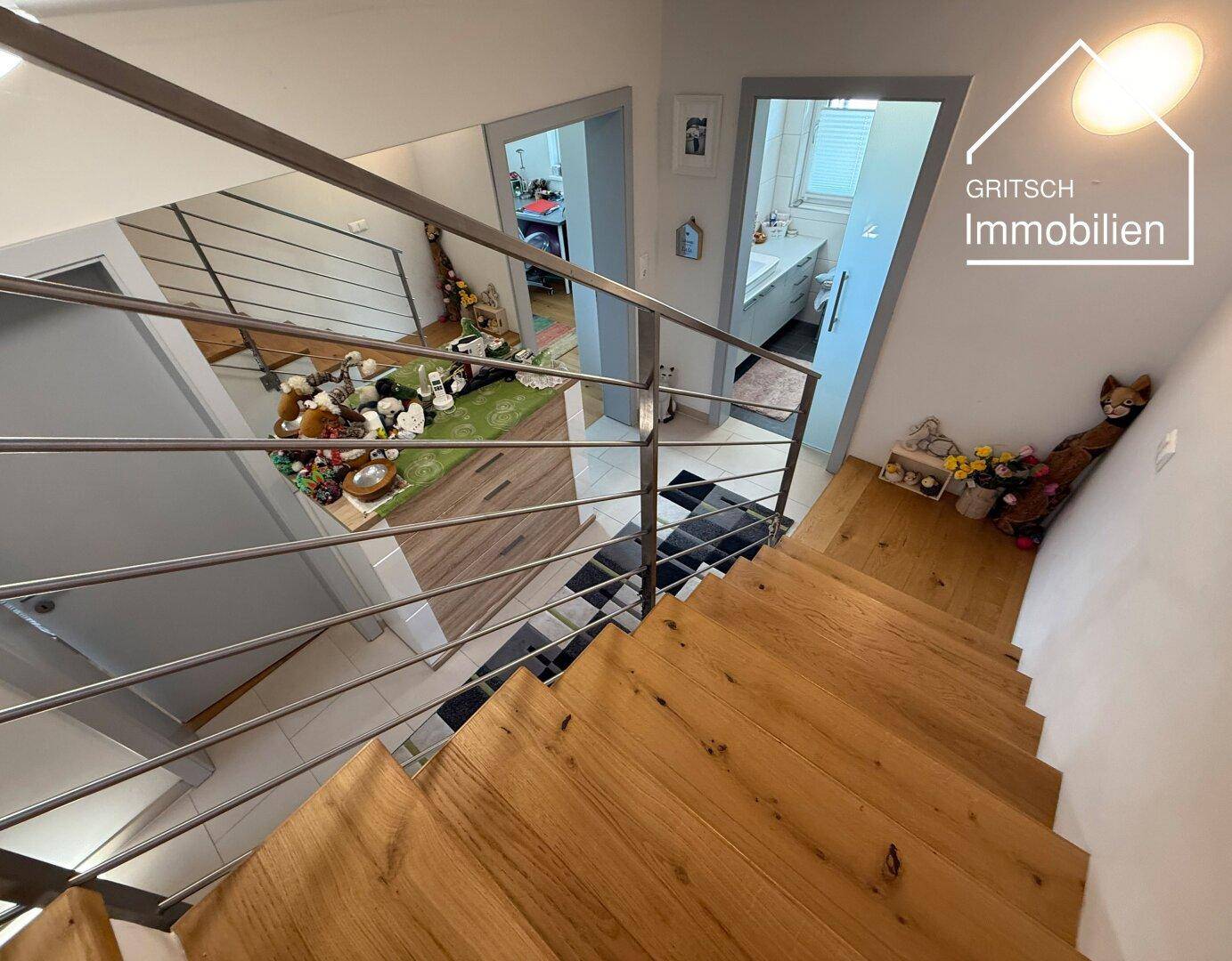 Holztreppe mit modernem Metallgeländer, die zu den oberen Etagen führt, mit Blick auf einen Flur.