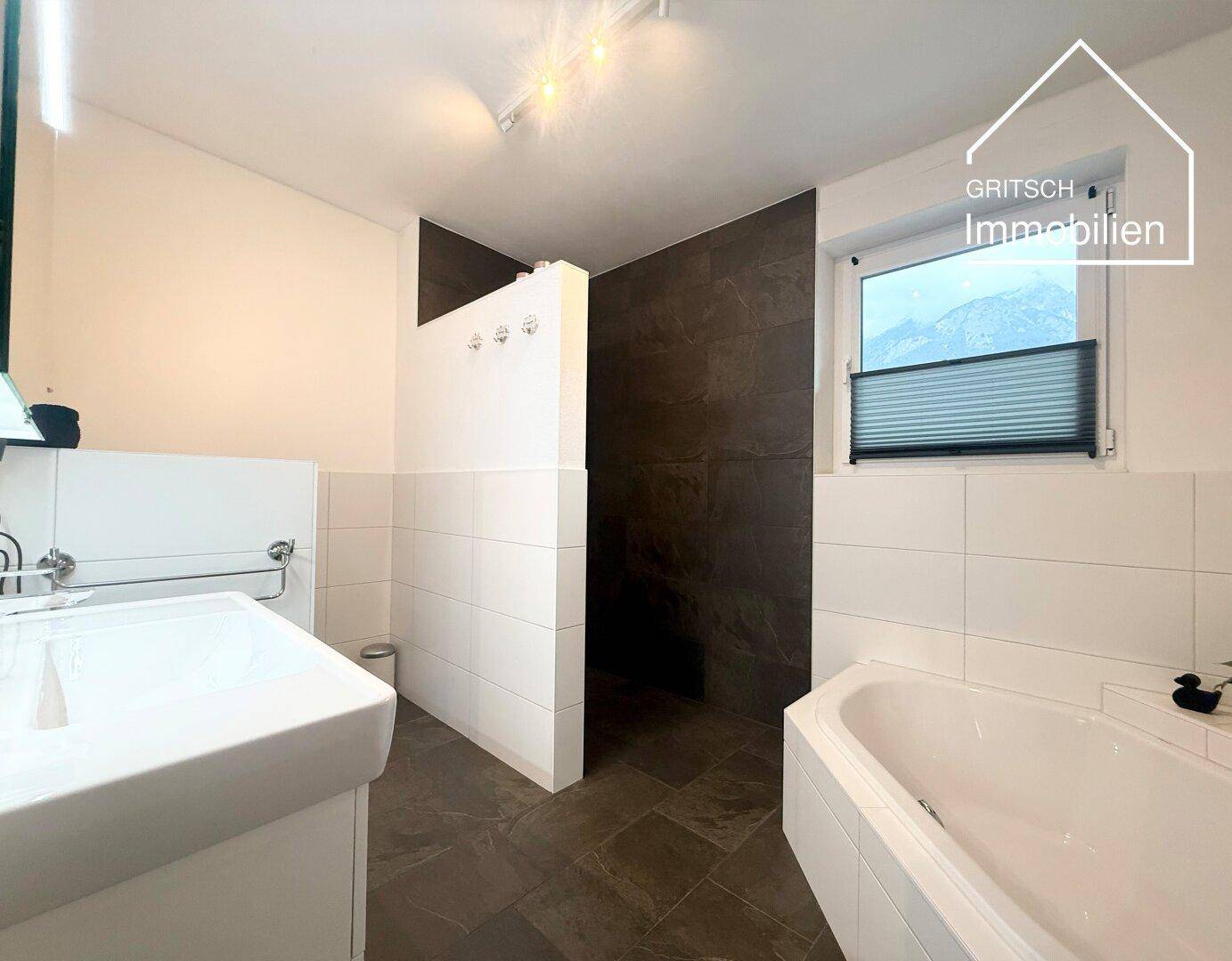 Modernes Badezimmer mit Badewanne, begehbarer Dusche und Fenster, ausgestattet mit dunklen und hellen Fliesen.