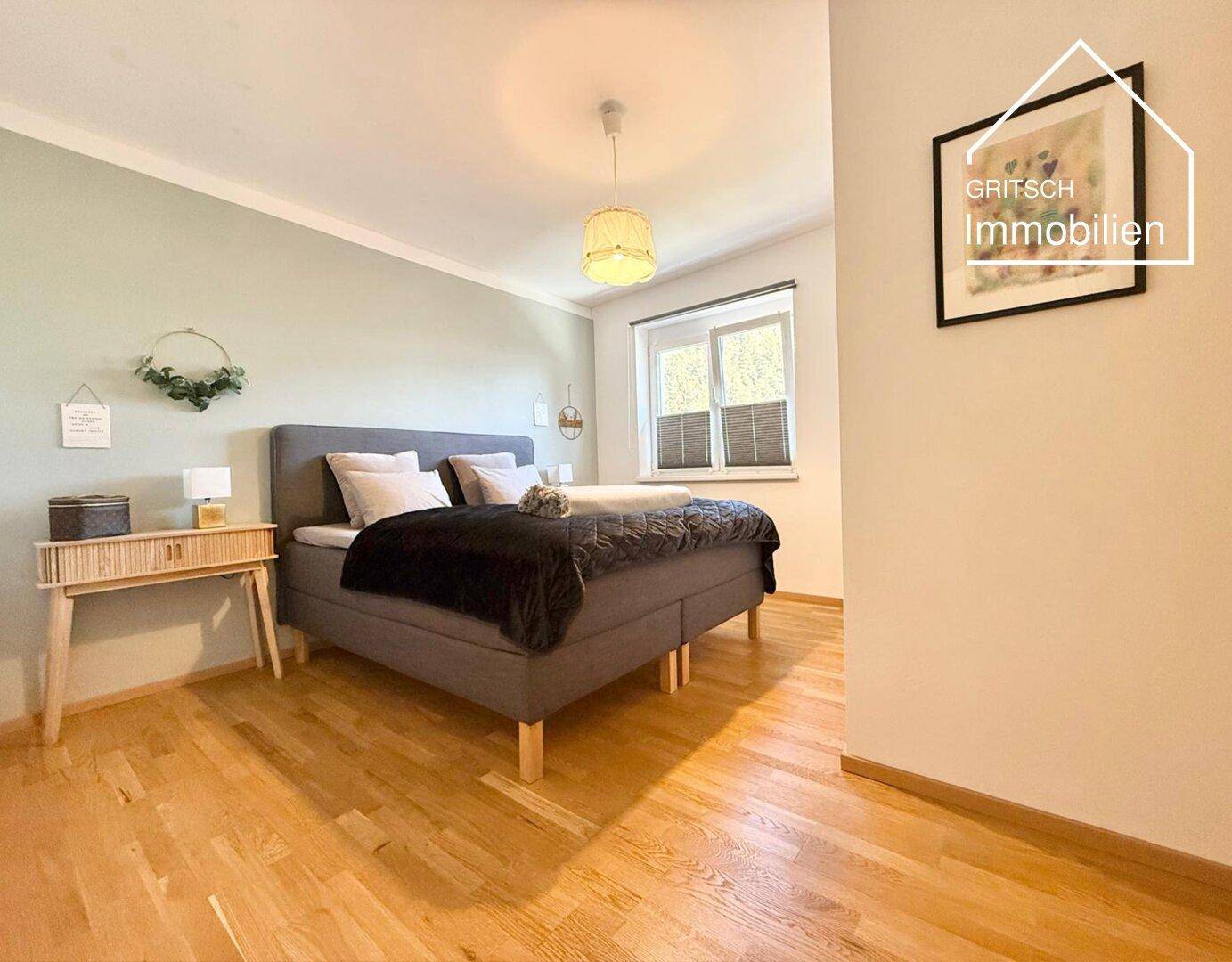 Helles Schlafzimmer mit Holzboden, großem Bett und Fenster, modern und gemütlich eingerichtet.