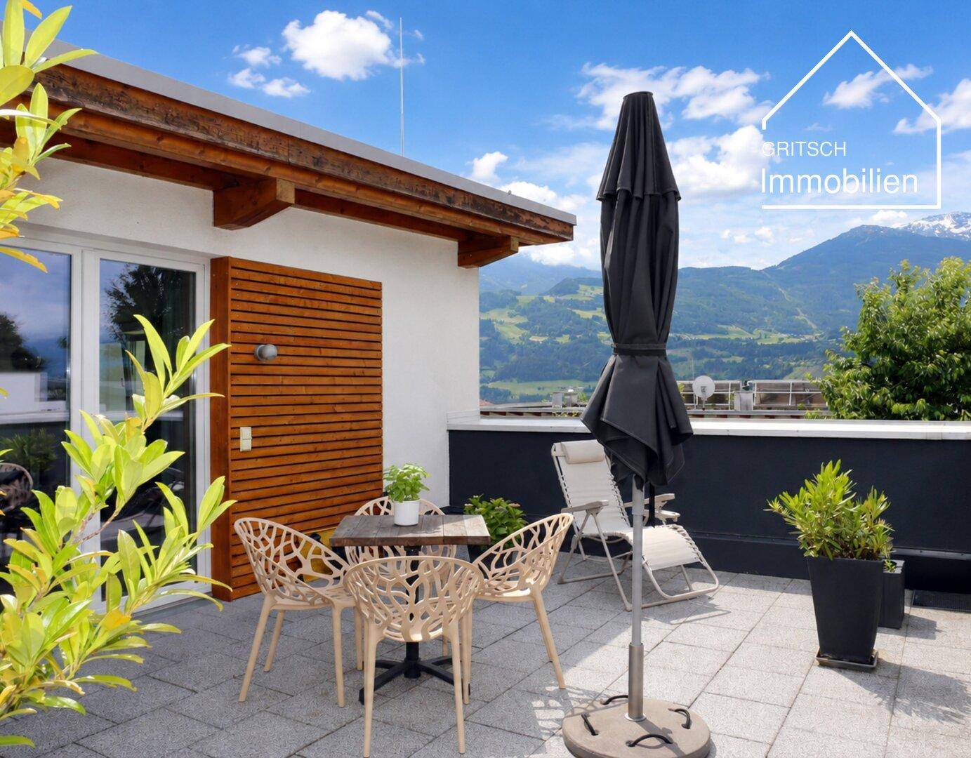Sonnige Dachterrasse mit Sitzgelegenheiten, Sonnenschirm und atemberaubendem Panoramablick auf die Berge.