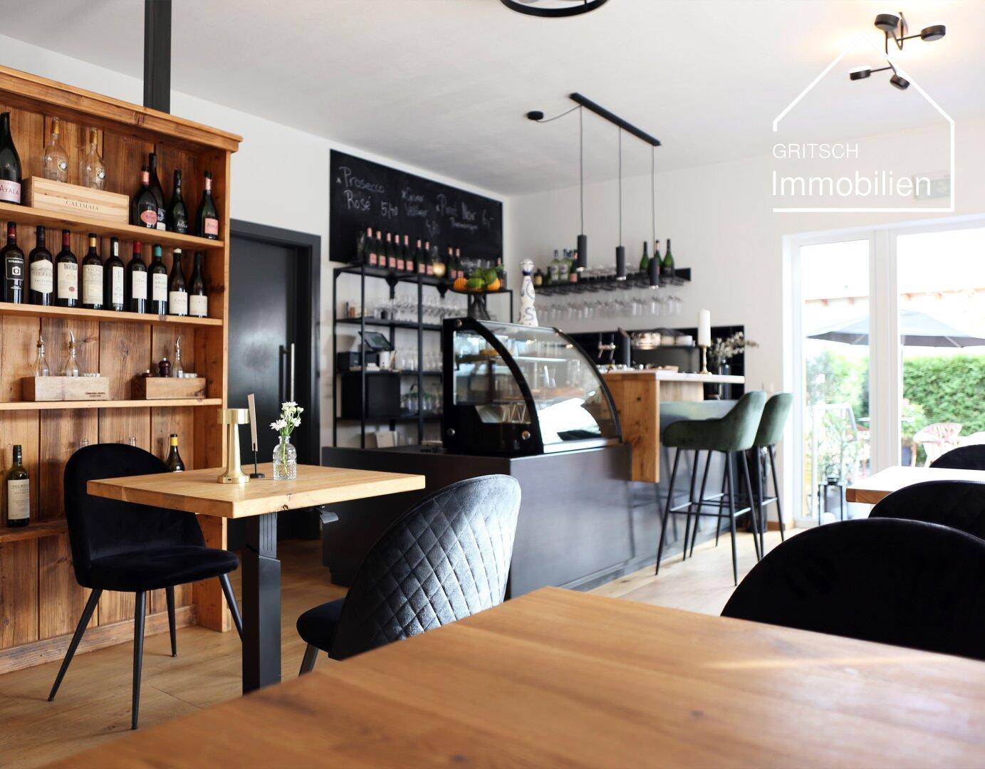 Innenansicht eines Gastronomiebereichs mit Weinflaschenregal, Bar und Sitzgelegenheiten.