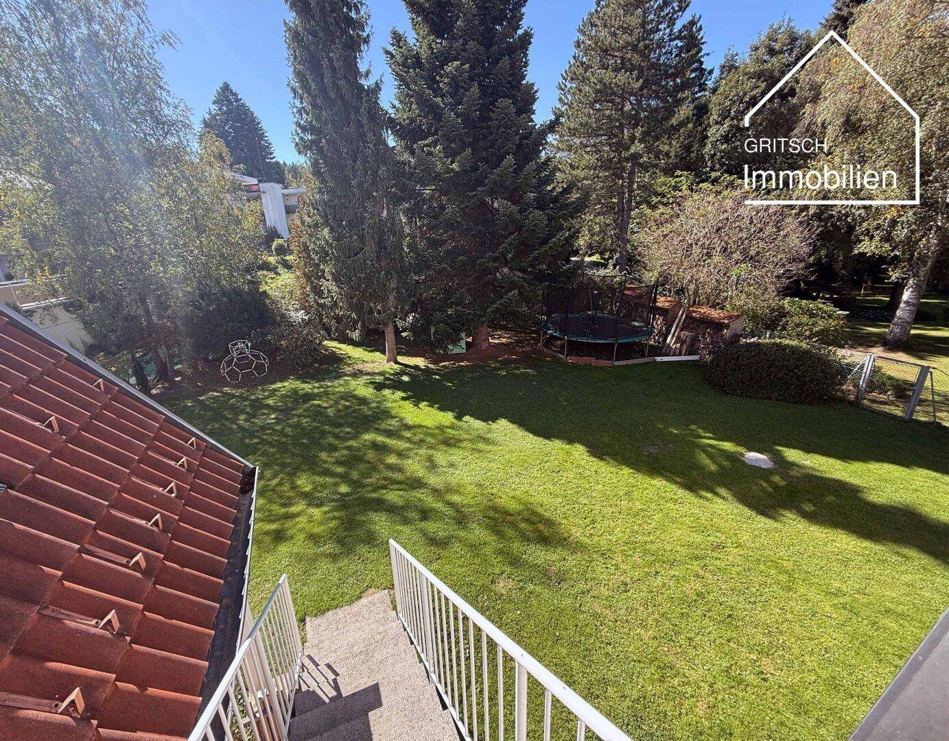 Großer, gepflegter Garten mit Rasenfläche, hohen Bäumen und einem Trampolin für Freizeitaktivitäten.