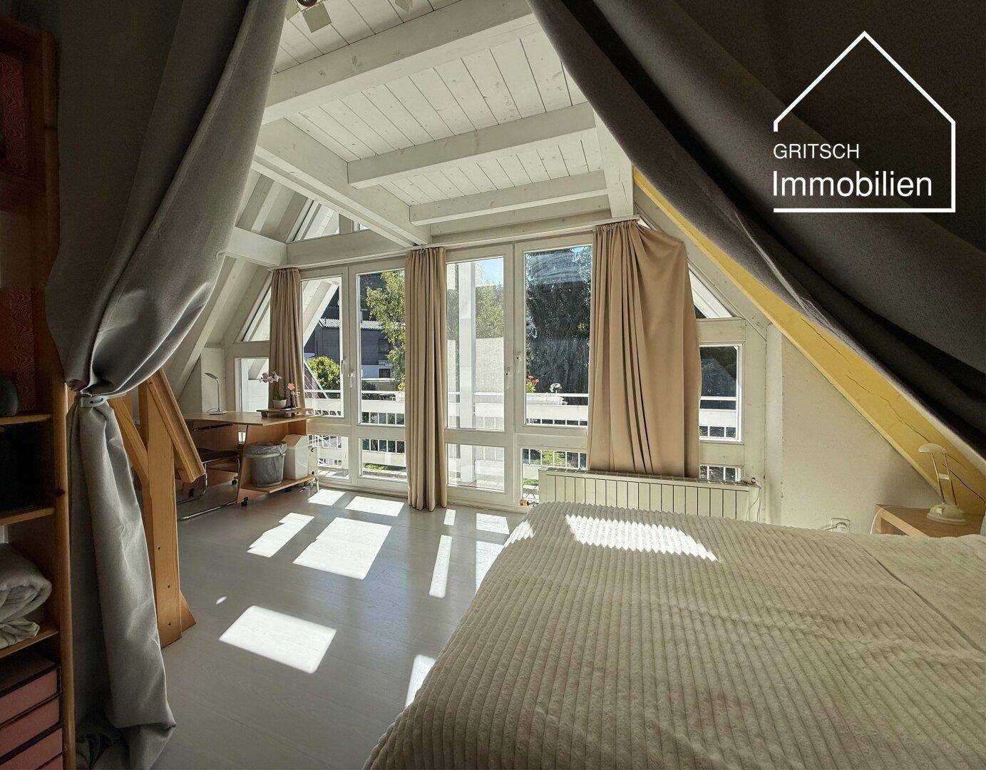 Gemütliches Schlafzimmer im Dachgeschoss mit schrägen Wänden, Holzbalken und Zugang zu einem Balkon.