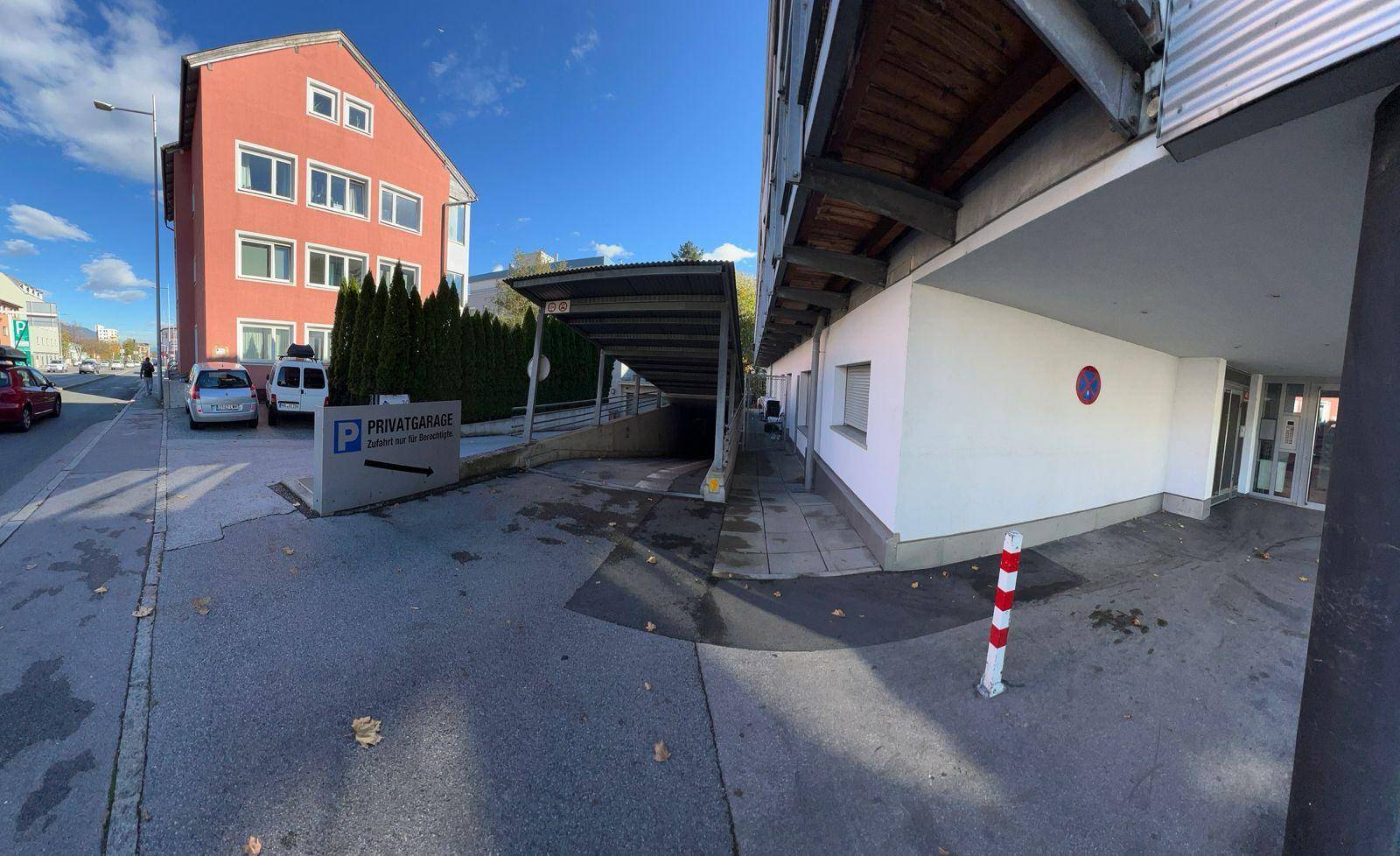 Eingangsbereich einer privaten Tiefgarage mit überdachter Zufahrt und umliegenden Gebäuden.