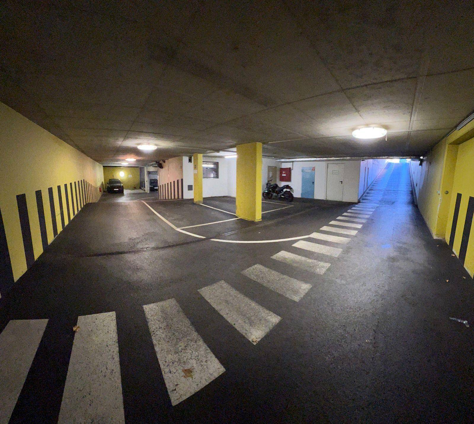 Geräumige Tiefgarage mit markierten Fahrspuren und Parkplätzen, beleuchtet von Deckenleuchten.