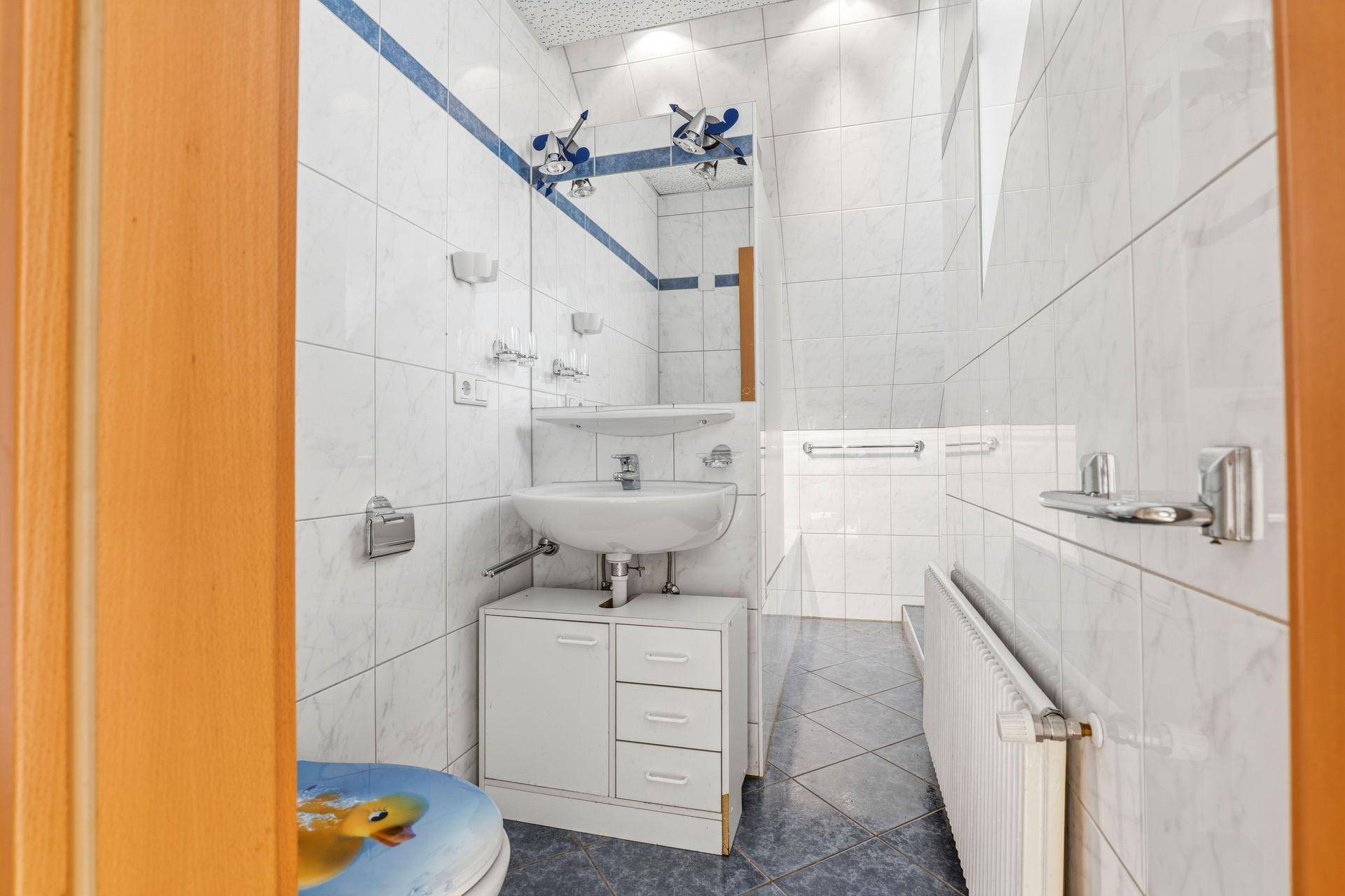 Gefliestes Badezimmer mit Waschbecken, Spiegel und blauen Akzenten.