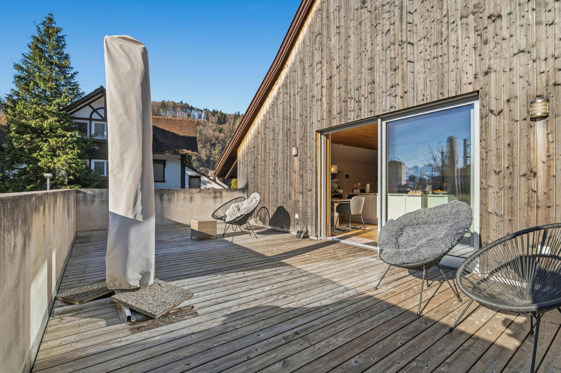 Sonniger Terrassenbereich mit Holzdeck, modernen Stühlen und Zugang zum Innenbereich.