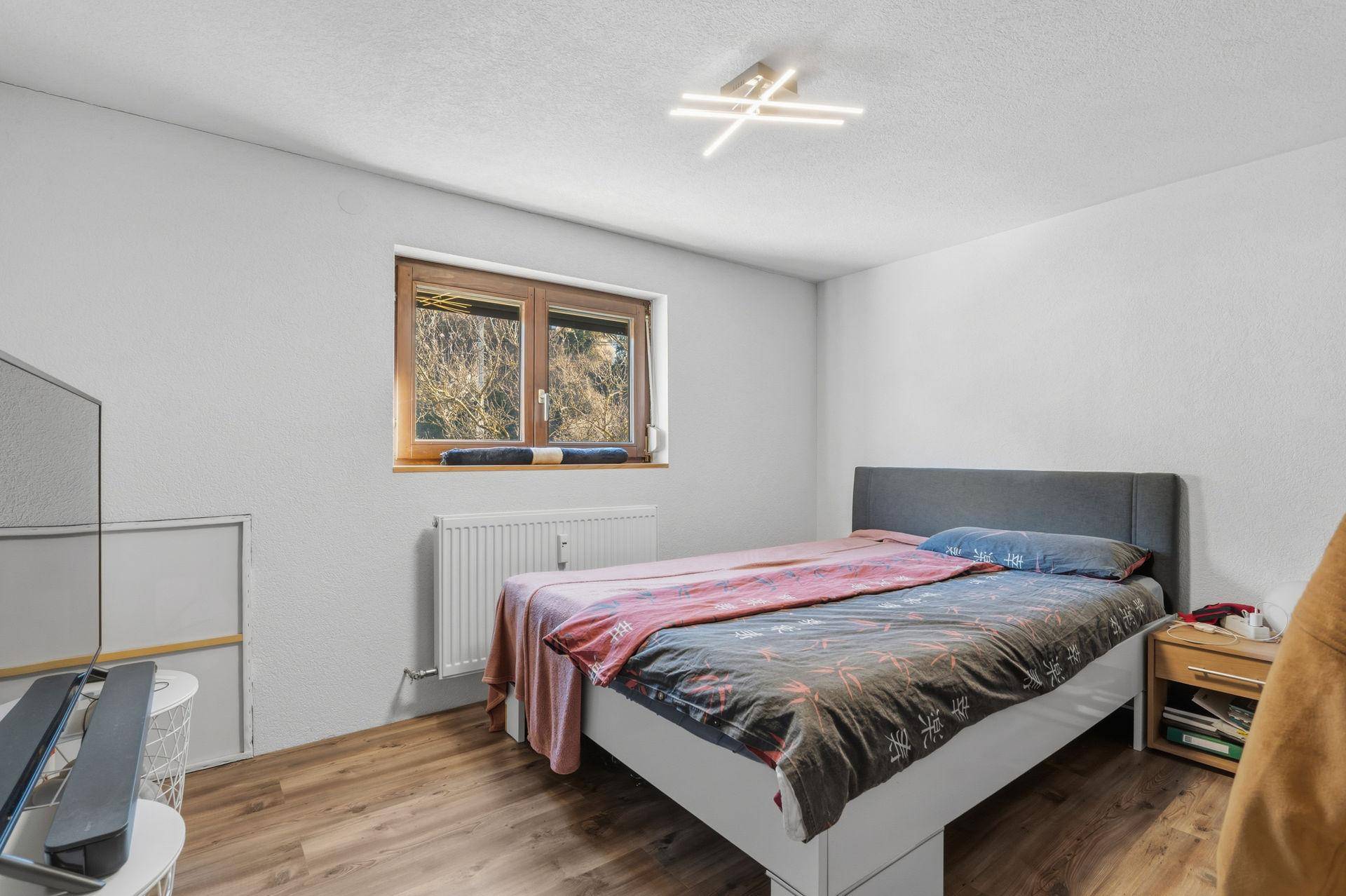 Gemütliches Schlafzimmer mit Holzboden, Fenster und Blick ins Grüne.
