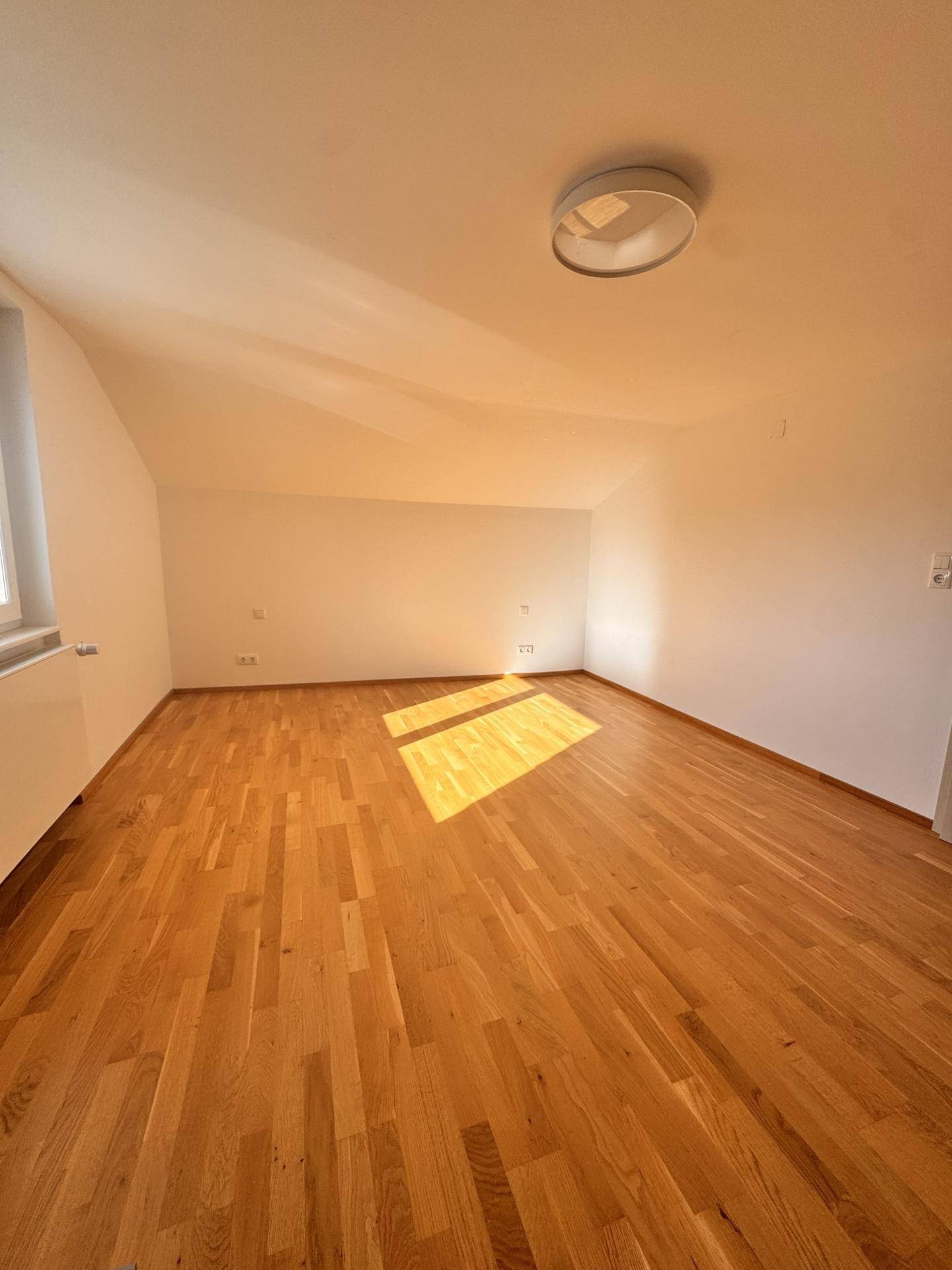 Helles Zimmer mit Holzboden und viel Tageslicht, bereit zur individuellen Gestaltung.