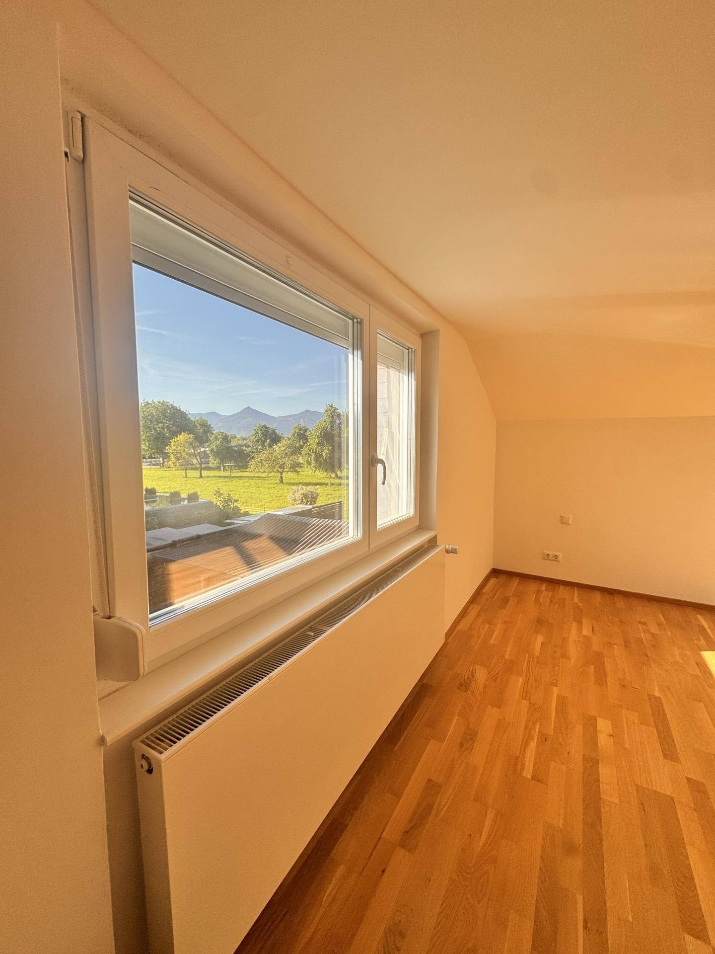Lichtdurchflutetes Zimmer mit weitem Blick auf die umliegende Berglandschaft und grüne Natur.