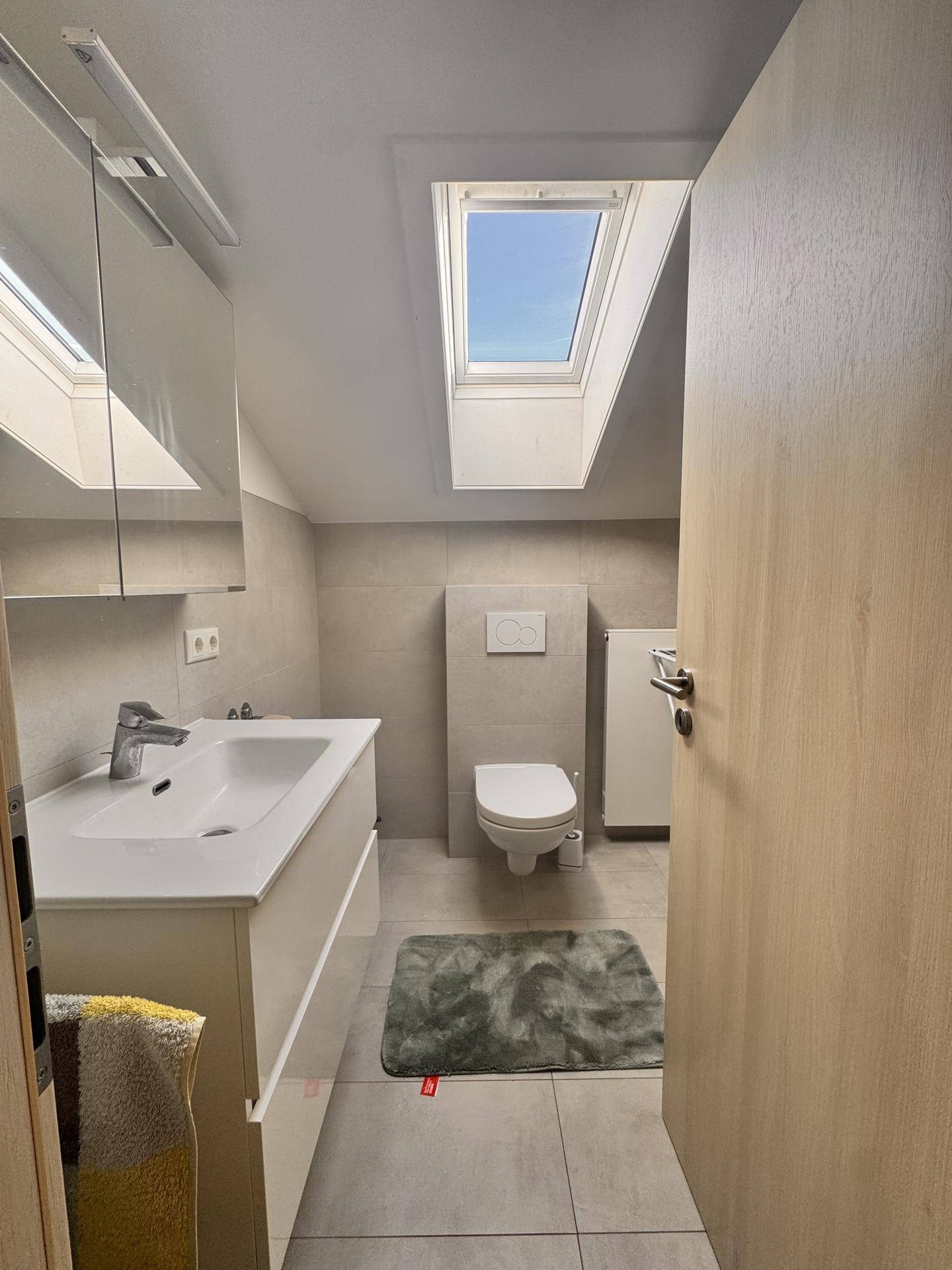 Modernes Badezimmer mit Dachfenster, Waschtisch und wandhängendem WC, hell und funktional.