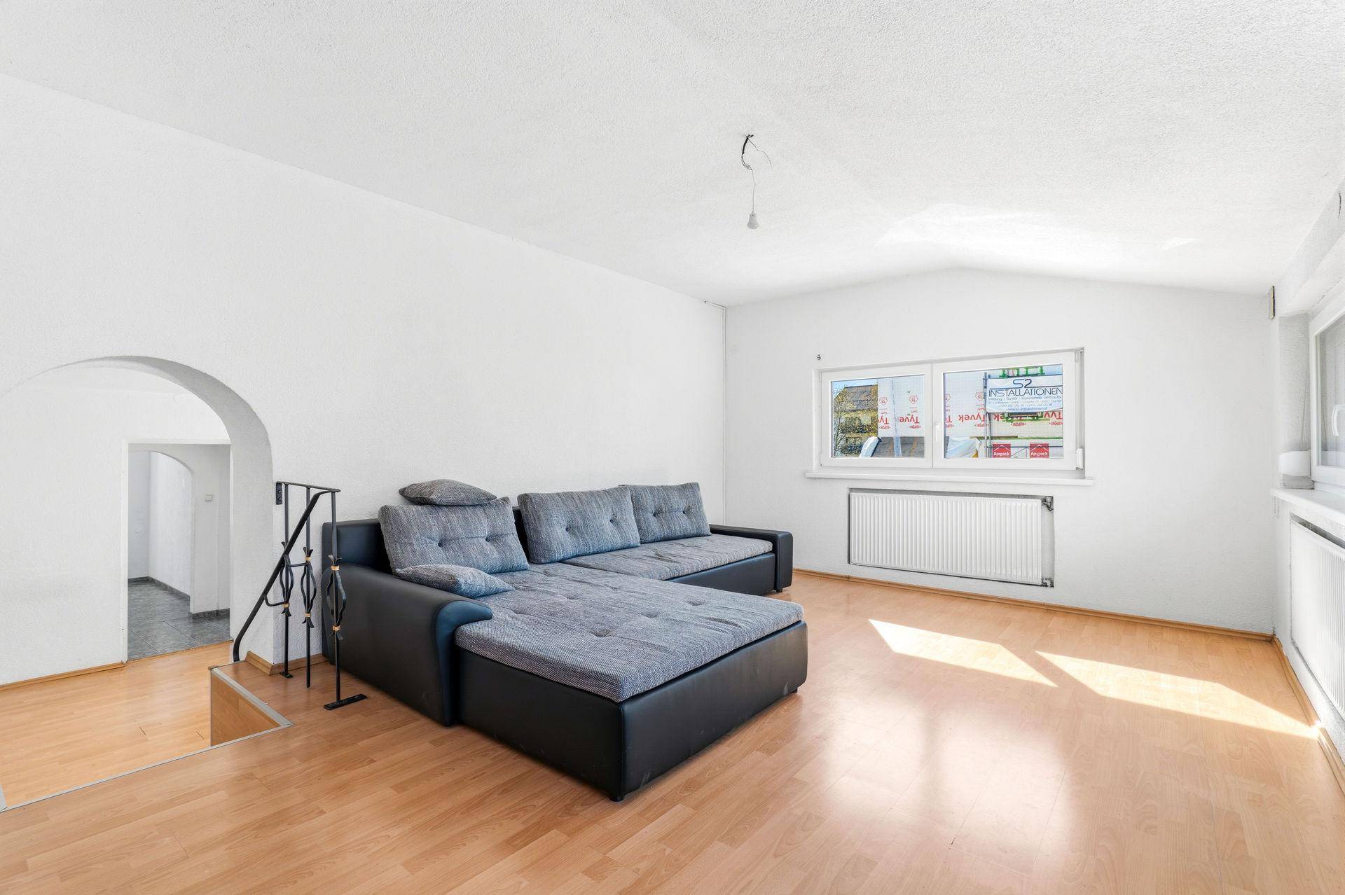 Wohnzimmer mit Parkettboden, großem Ecksofa und mehreren Fenstern für viel Licht.