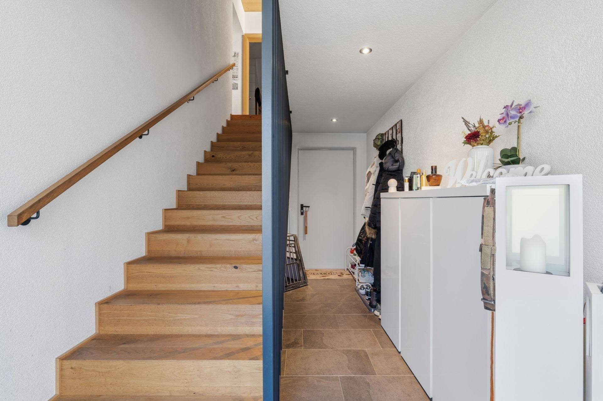 Heller Eingangsbereich mit Holztreppe und modernem Geländer.