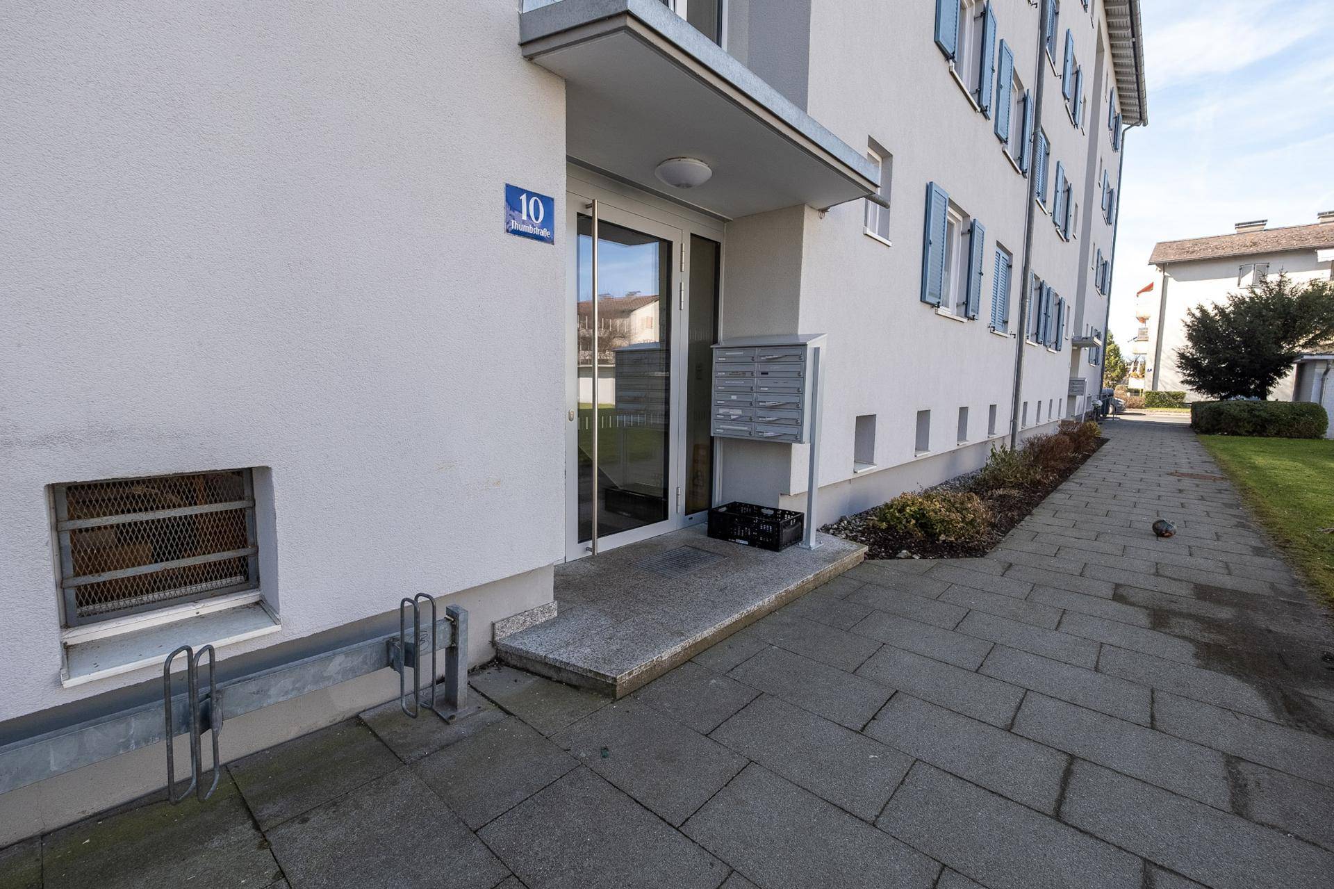 Eingangsbereich eines Mehrfamilienhauses mit Hausnummer, Briefkästen und gepflastertem Zugang.