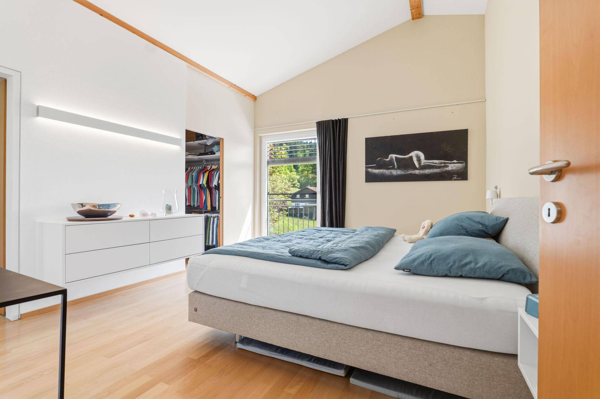 Helles Schlafzimmer mit Bett, integriertem Kleiderschrank und Holzboden.
