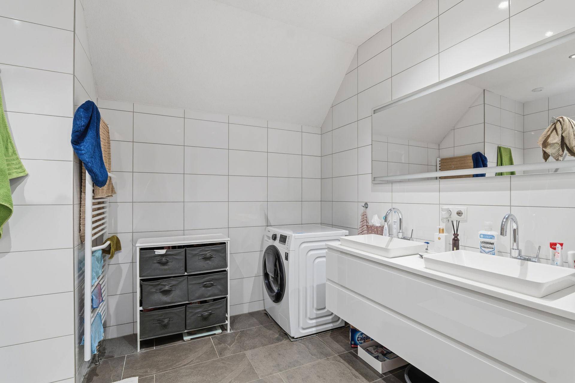 Geräumiges Badezimmer mit Doppelwaschbecken, Waschmaschine und beheiztem Handtuchhalter.