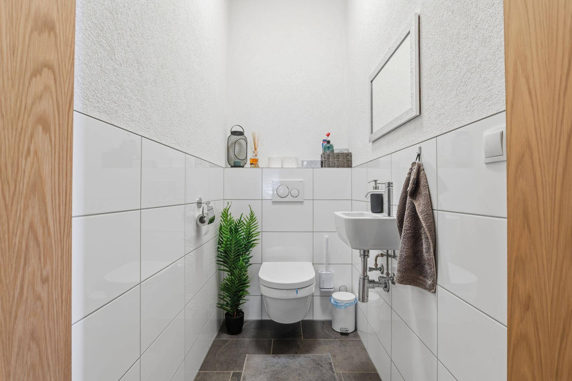 Kleines Gäste-WC mit Wand-WC, Waschbecken und modernen weißen Fliesen.