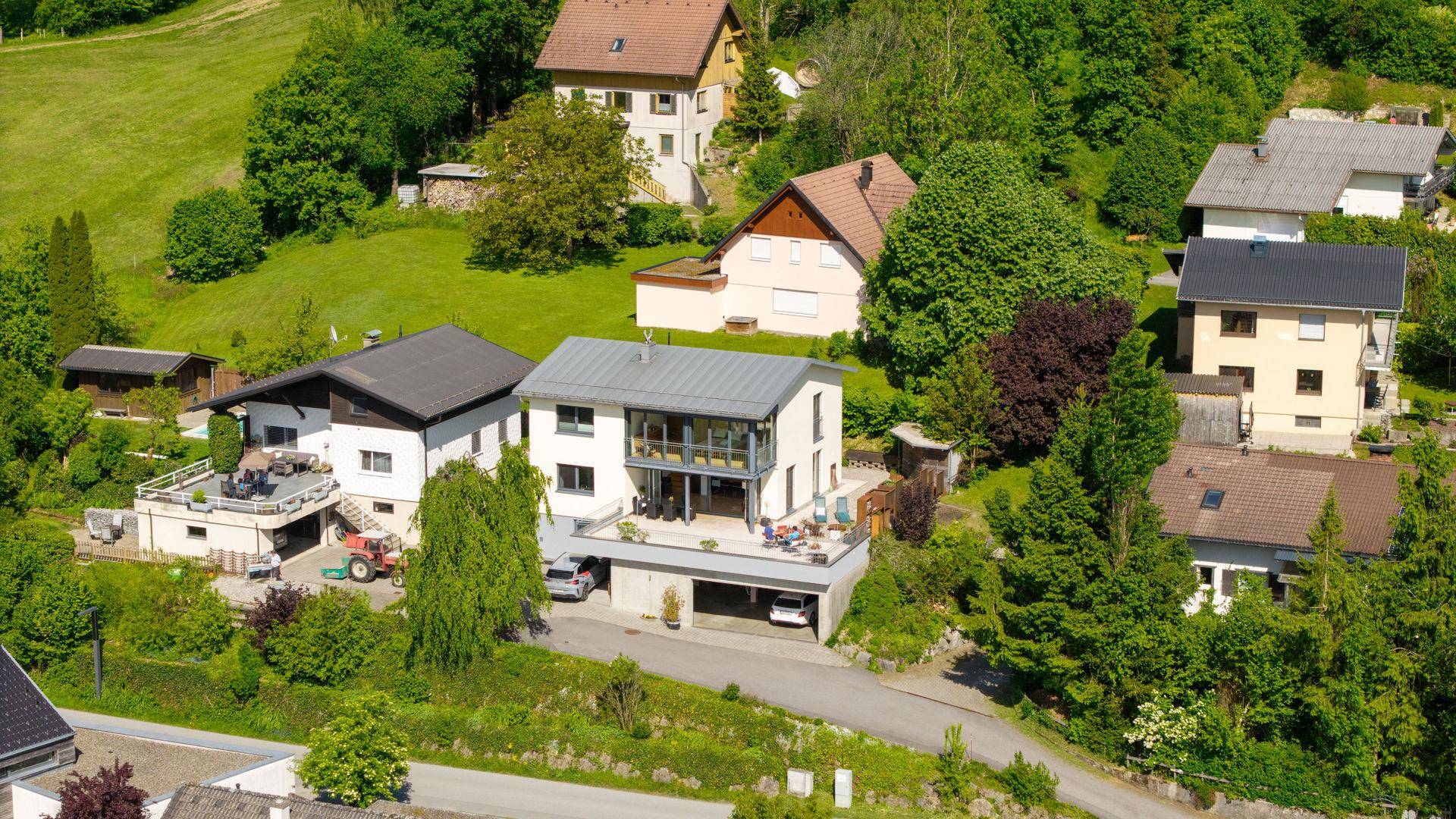 Luftaufnahme einer Wohnsiedlung mit mehreren Häusern und grünen Hügeln in ländlicher Umgebung.