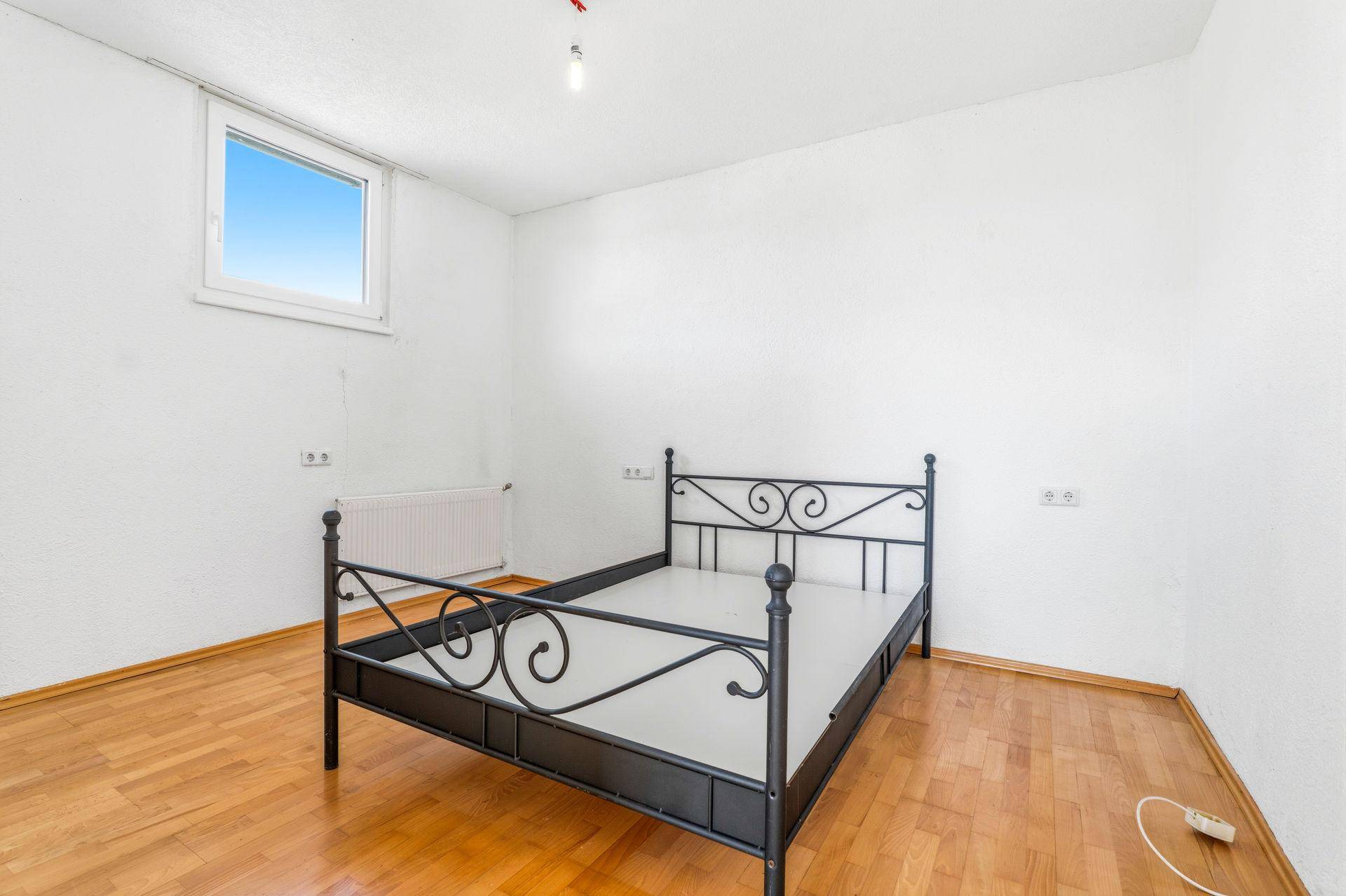 Schlafzimmer mit Parkettboden, Fenster und einem schmiedeeisernen Bettgestell.